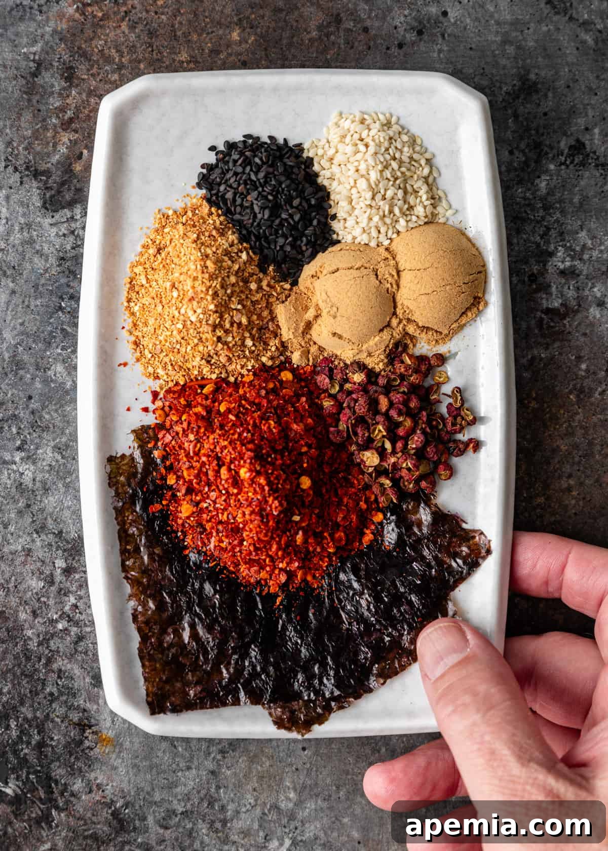 Overhead shot displaying all the essential ingredients laid out neatly on a kitchen counter: chili flakes, Sichuan peppercorns, dried orange peel, nori, ginger, and sesame seeds, ready for blending.