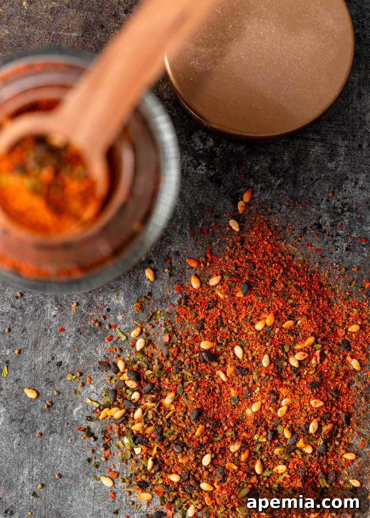 Close-up shot of Shichimi Togarashi spice blend artfully spread on a counter with a spice jar visible to the left, highlighting its fine texture and rich colors.