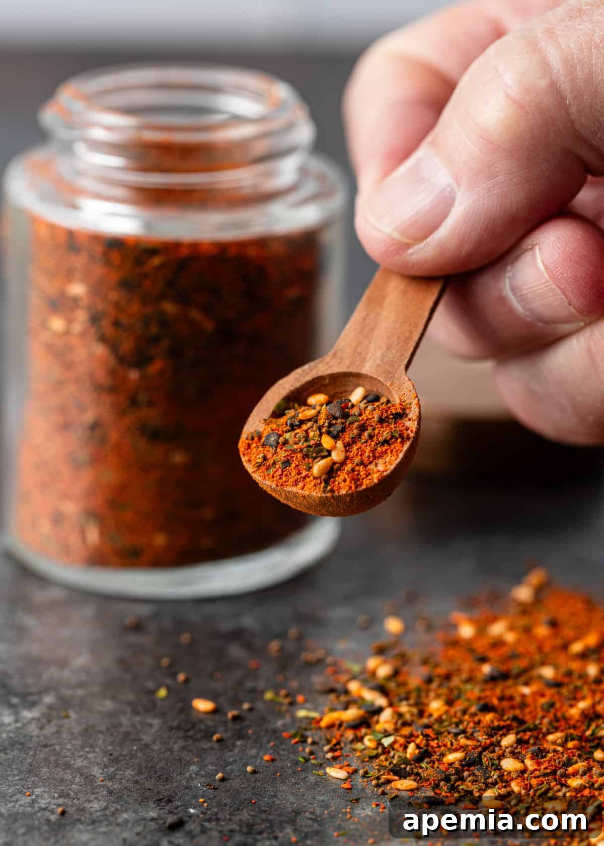 A hand gracefully lifting a small wooden spoon, laden with a generous portion of freshly made Shichimi Togarashi, poised to be sprinkled onto a delicious dish.