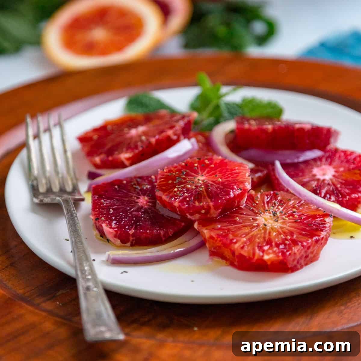 A plate of blood orange salad with thinly sliced red onion and fresh mint leaves visible, showcasing its vibrant colors.
