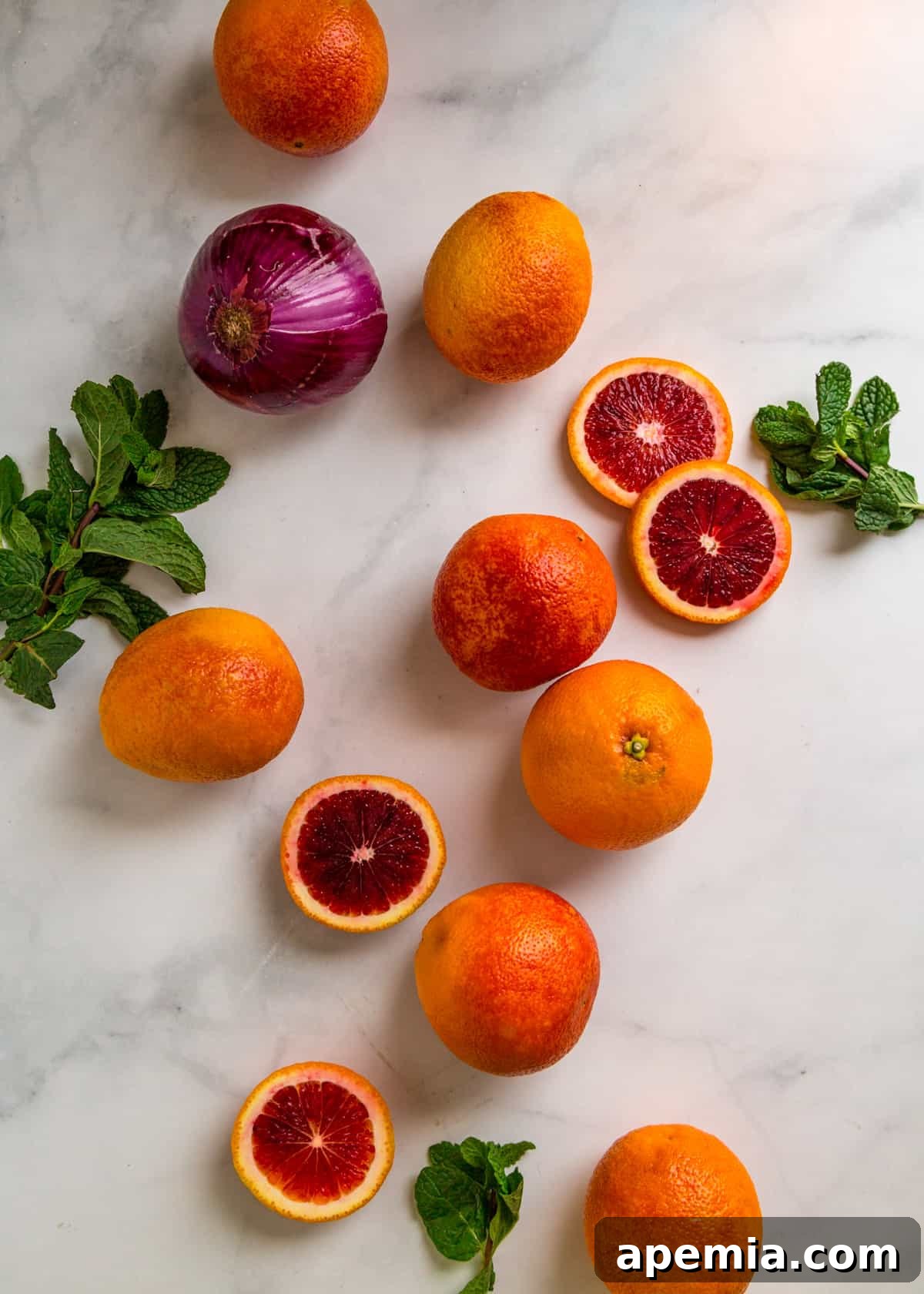 Overhead view of fresh blood oranges, a red onion, and sprigs of mint, ready for preparing blood orange salad.