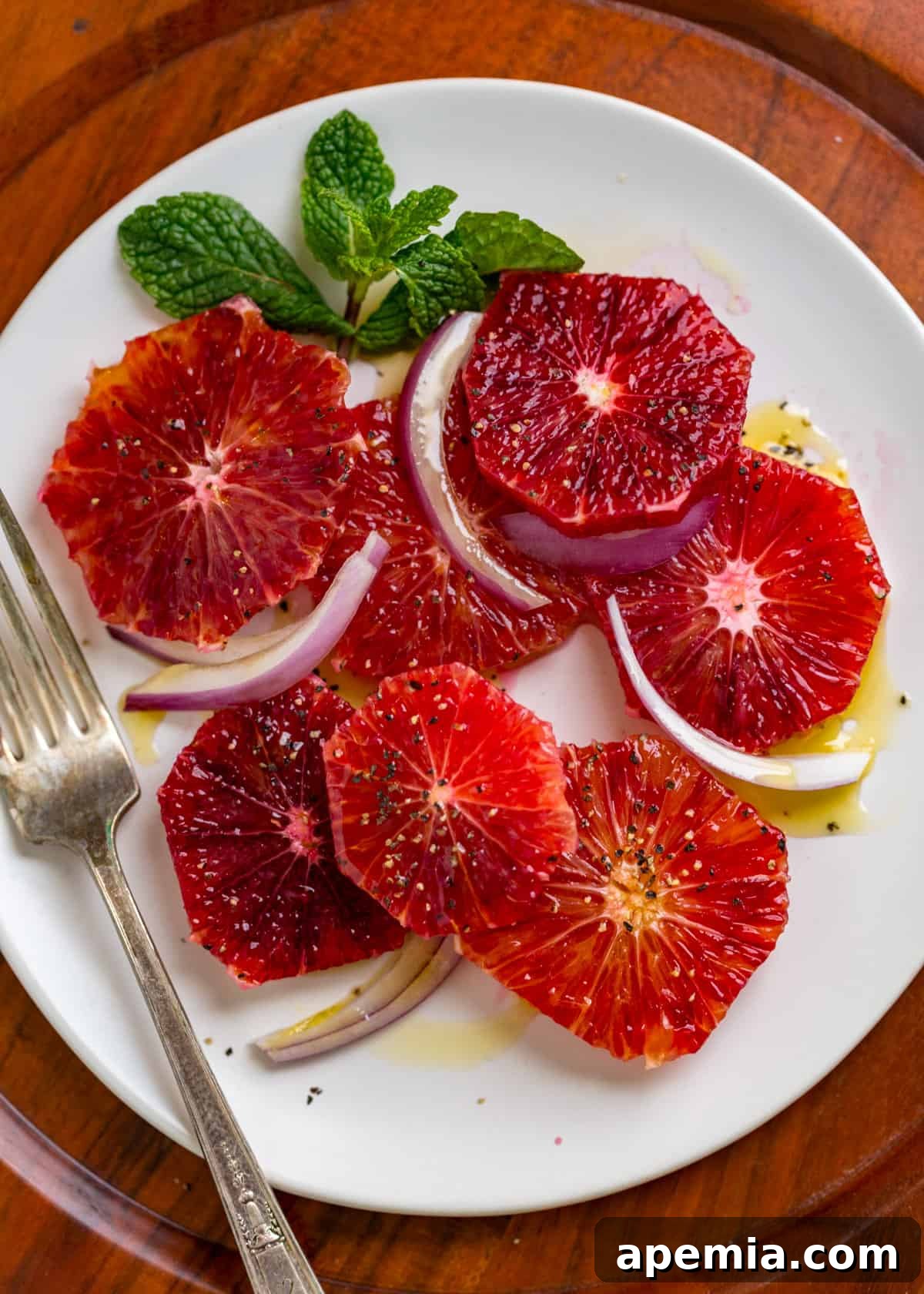 Overhead view of my blood orange salad recipe elegantly presented on a plate, featuring visible red onion, a generous drizzle of olive oil, and fresh mint leaves.