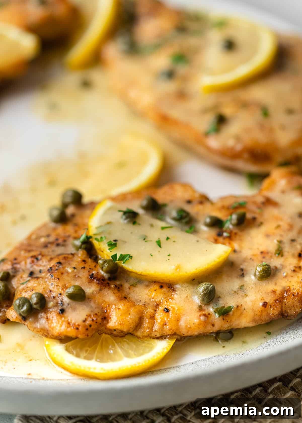 Zesty Lemon Caper Chicken 3 Close-up view of a perfectly cooked chicken piccata cutlet covered in a glistening lemon and caper sauce on a white plate.