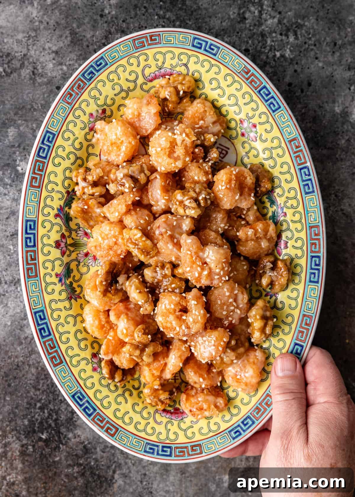 Golden Honey Walnut Shrimp 11 Overhead view: A hand holding a large Asian ceramic platter overflowing with freshly made honey walnut shrimp, ready to be served.