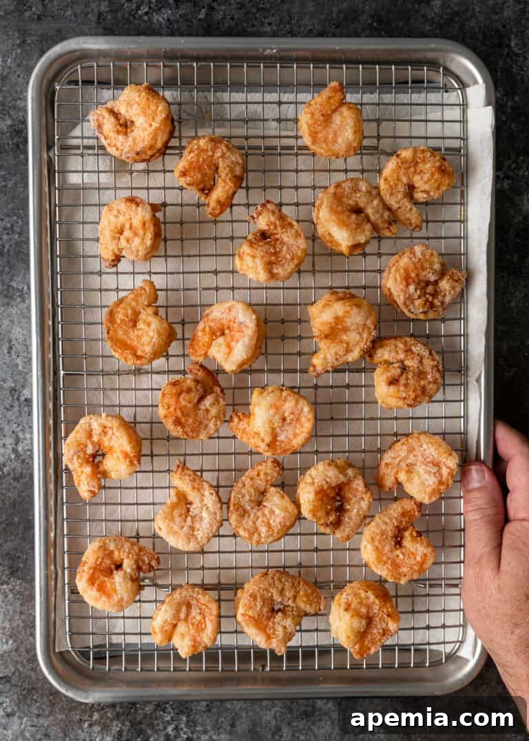 Golden Honey Walnut Shrimp 8 Overhead process shot: Freshly fried, crispy shrimp resting on a wire rack set over a baking sheet lined with parchment paper, draining excess oil.