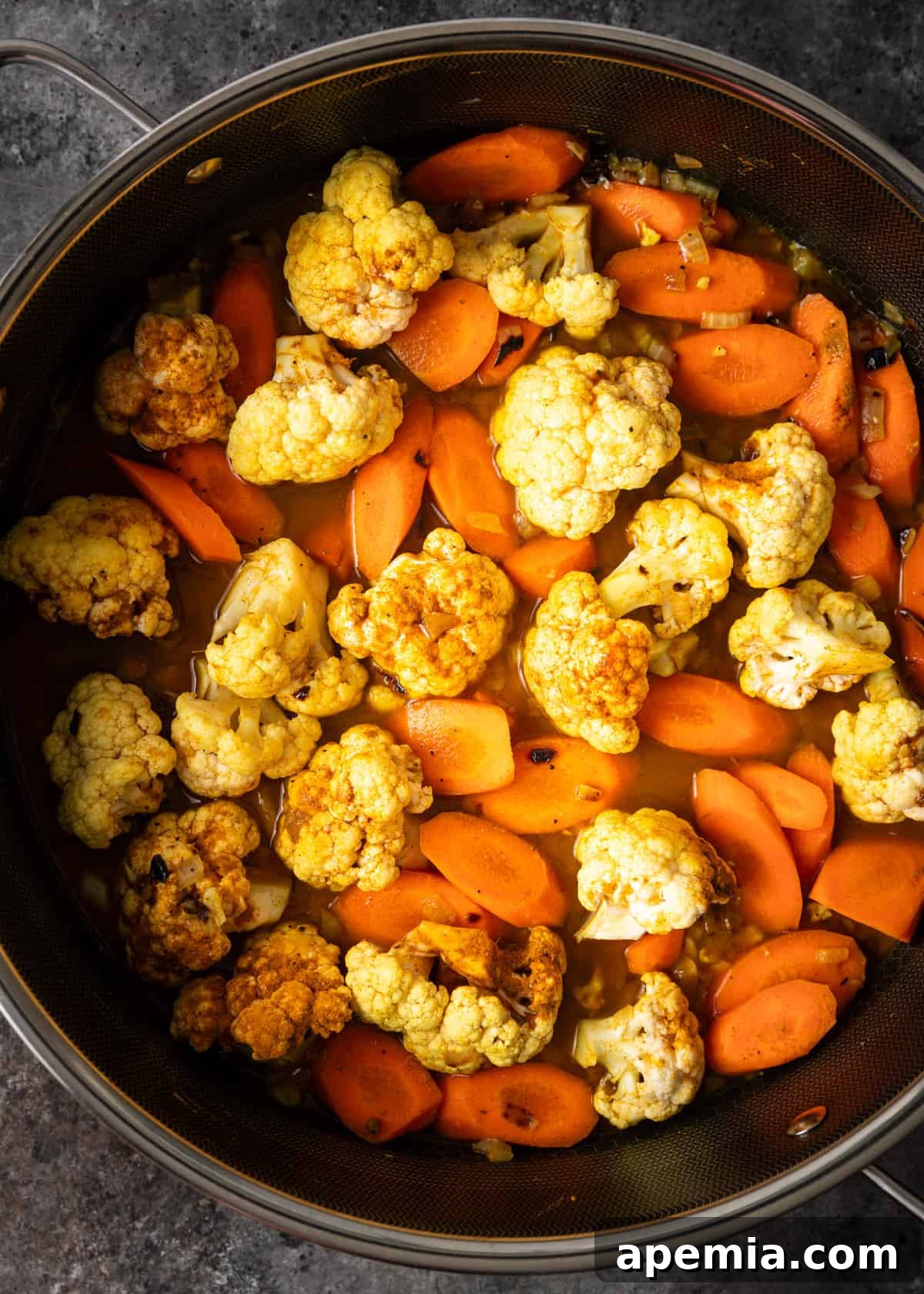 Moroccan Cauliflower and Carrot Tagine 5 Overhead shot of cauliflower and carrots gently cooking in a large saucepan, aromatic spices being stirred in.