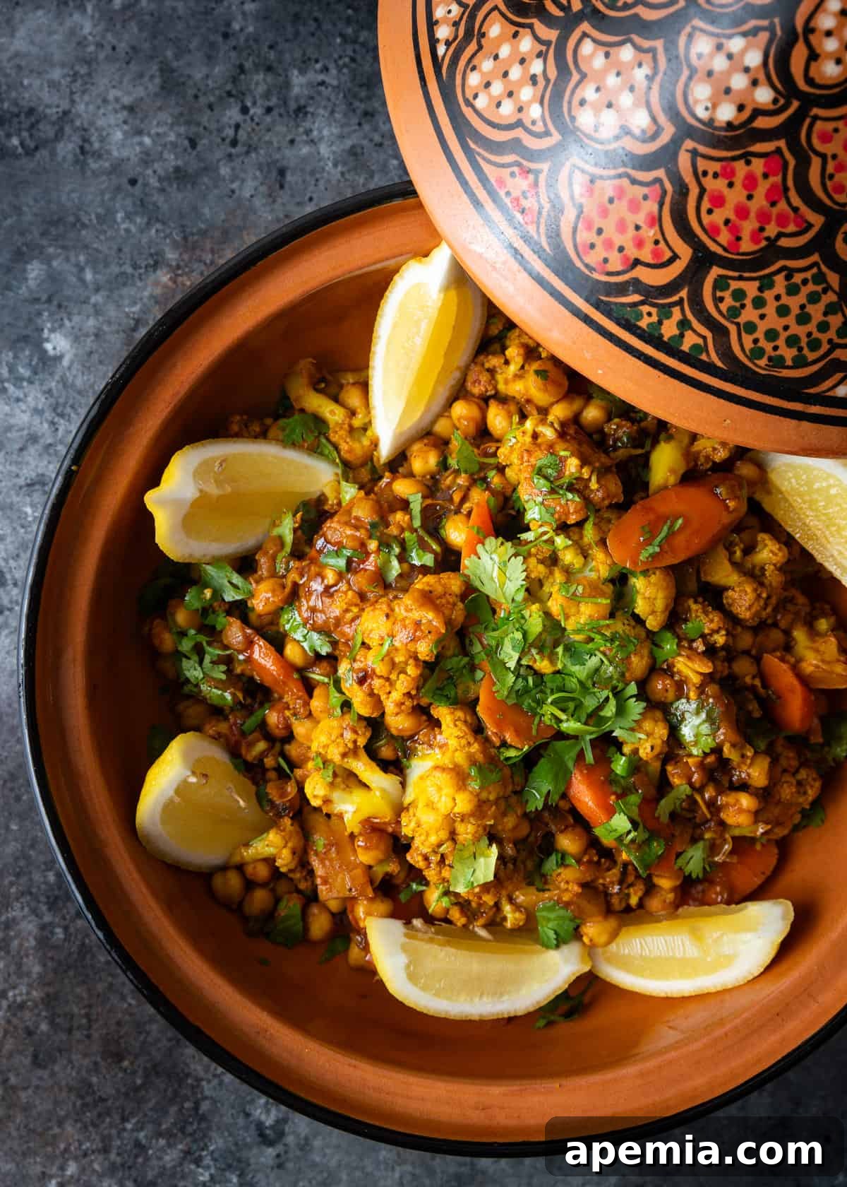Moroccan Cauliflower and Carrot Tagine 6 Overhead view of the finished Moroccan vegetable tagine, elegantly presented in a ceramic dish with lemon wedges and fresh herbs.