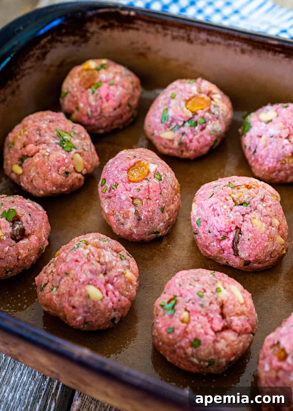 Process shot: Raw Roman style meatballs with visible raisins and pine nuts, arranged on a baking sheet before cooking.
