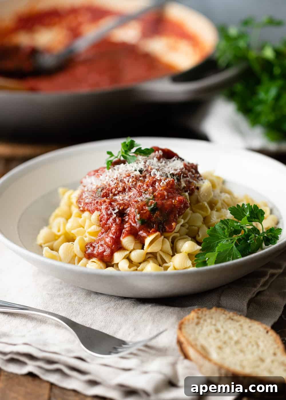 a bowl of pasta with sugo all'arrabiata and fresh herbs with a fork and piece of bread to the side