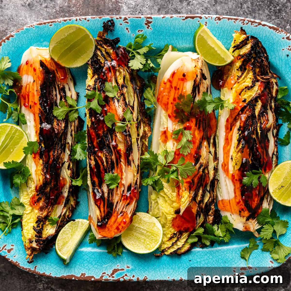 Sweet Chili Glazed Grilled Cabbage 2 Overhead shot of beautifully grilled cabbage quarters on a blue platter, generously smothered in sweet chili sauce and garnished with fresh herbs and lime wedges.