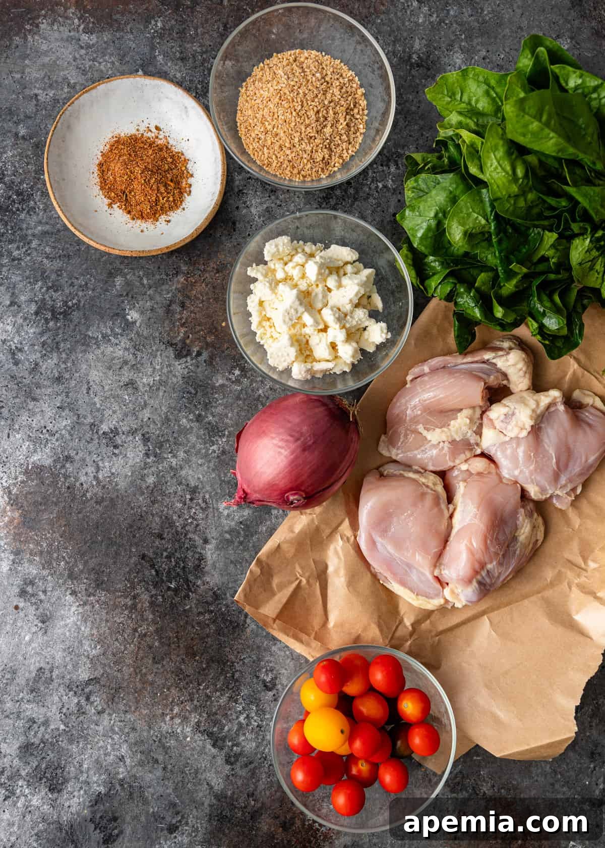 Overhead view of all the fresh ingredients laid out for preparing the Turkish chicken recipe, including chicken thighs, bulgur, various vegetables, and spice jars.