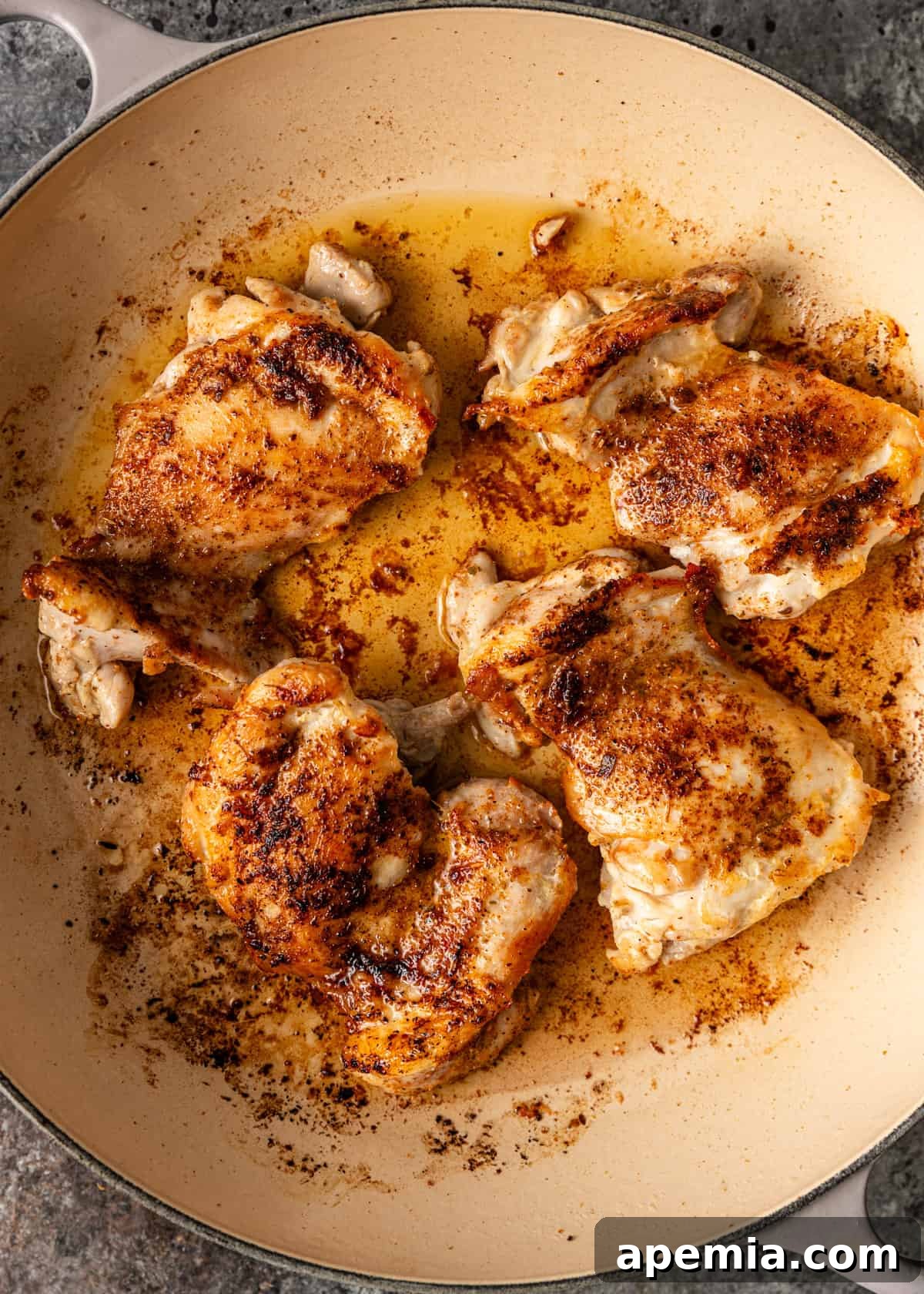 Close-up of browned chicken thighs in a skillet, perfectly seared with a golden crust, prior to baking.