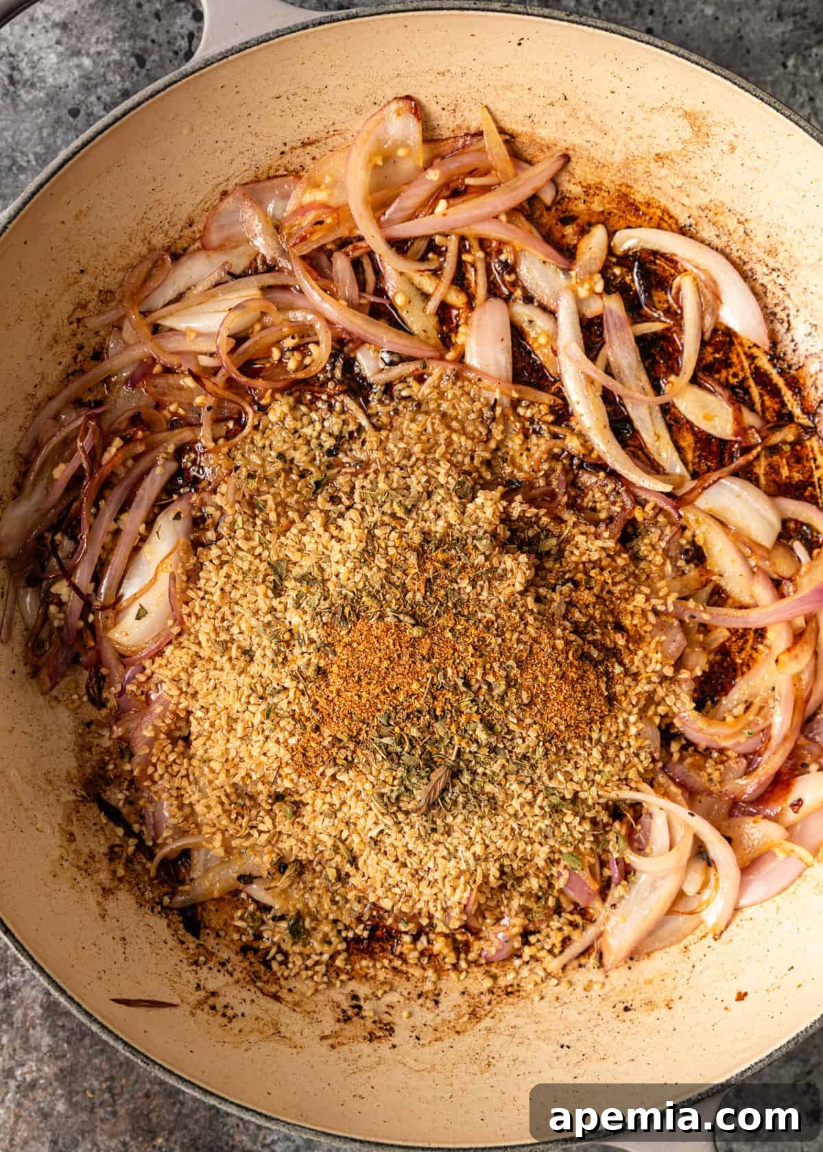 Sautéed onions with bulgur wheat and oregano in a skillet, aromatically cooking on the stovetop, releasing their fragrant oils.