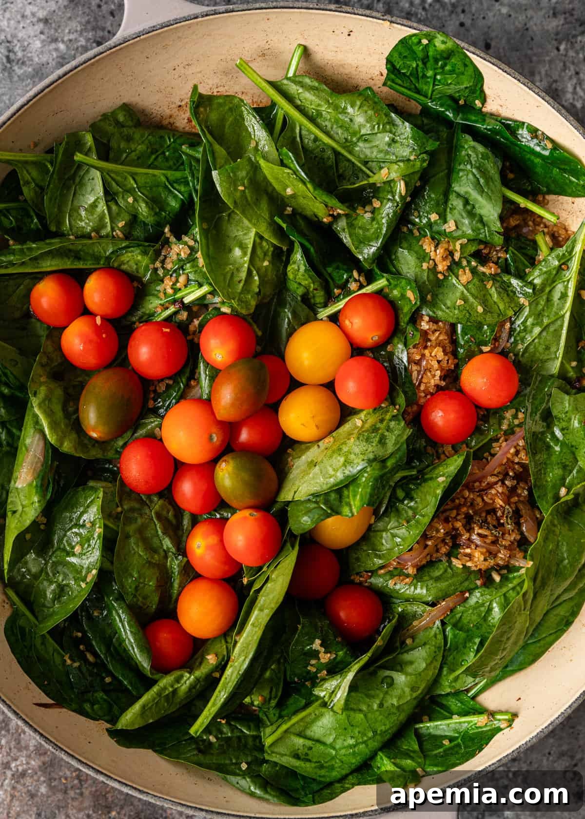 Wilted spinach and softened cherry tomatoes being stirred into the bulgur mixture in the skillet, adding color and freshness.