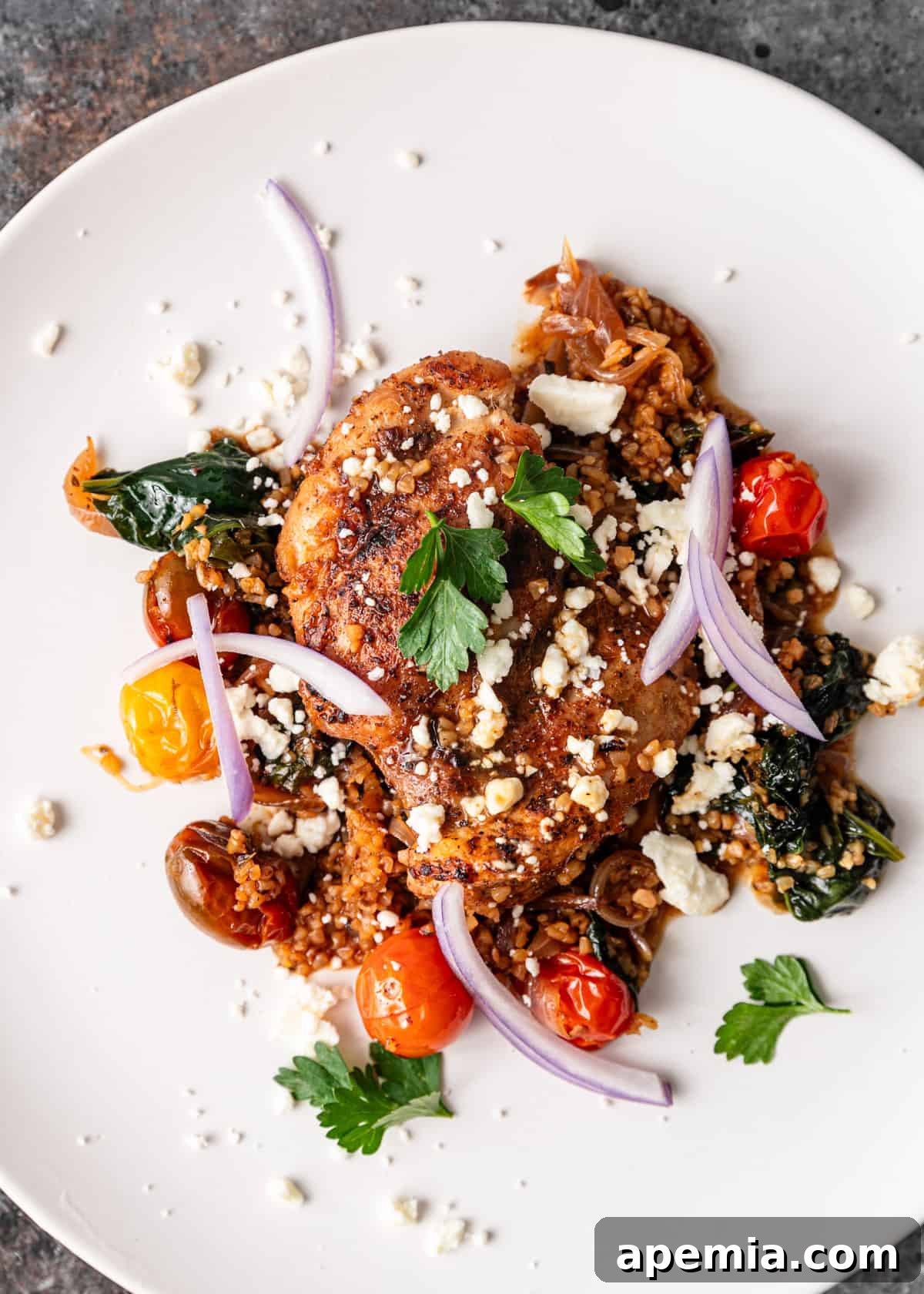 Turkish chicken dish on a white plate, garnished with crumbled feta, fresh parsley, and thinly sliced red onion, ready for serving.