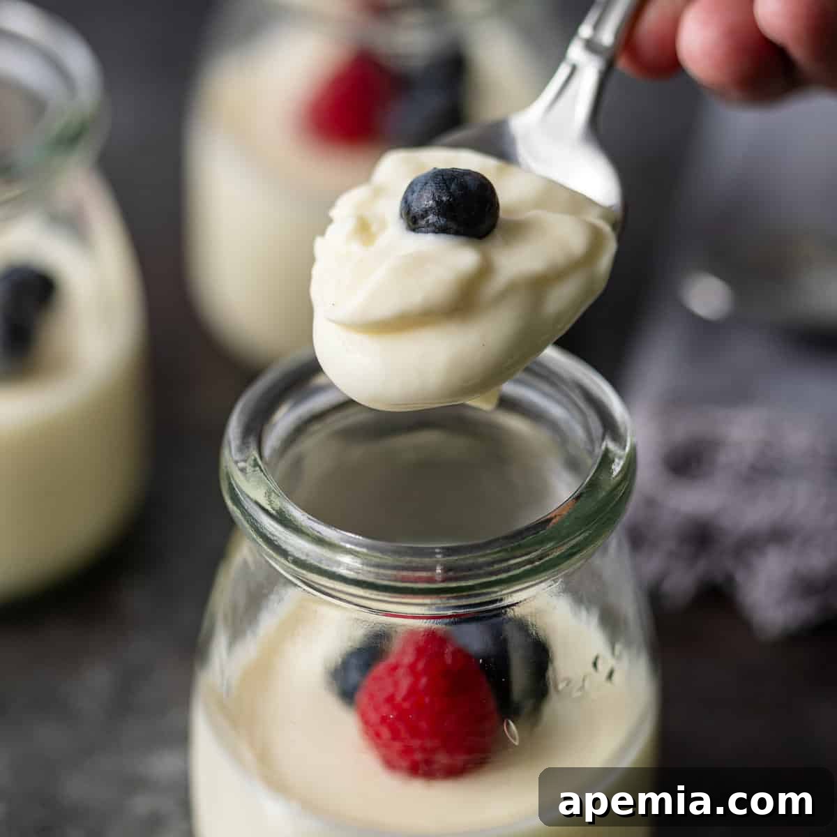 Zesty Creamy Lemon Posset 2 Closeup of a spoon lifting lemon posset from a glass jar, highlighting its creamy texture.