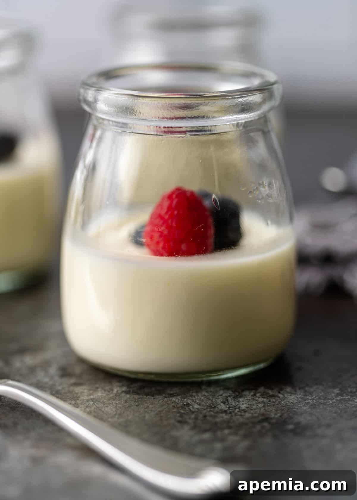 Zesty Creamy Lemon Posset 3 Side view of lemon posset served in a small glass jar, garnished with fresh raspberries and blueberries.