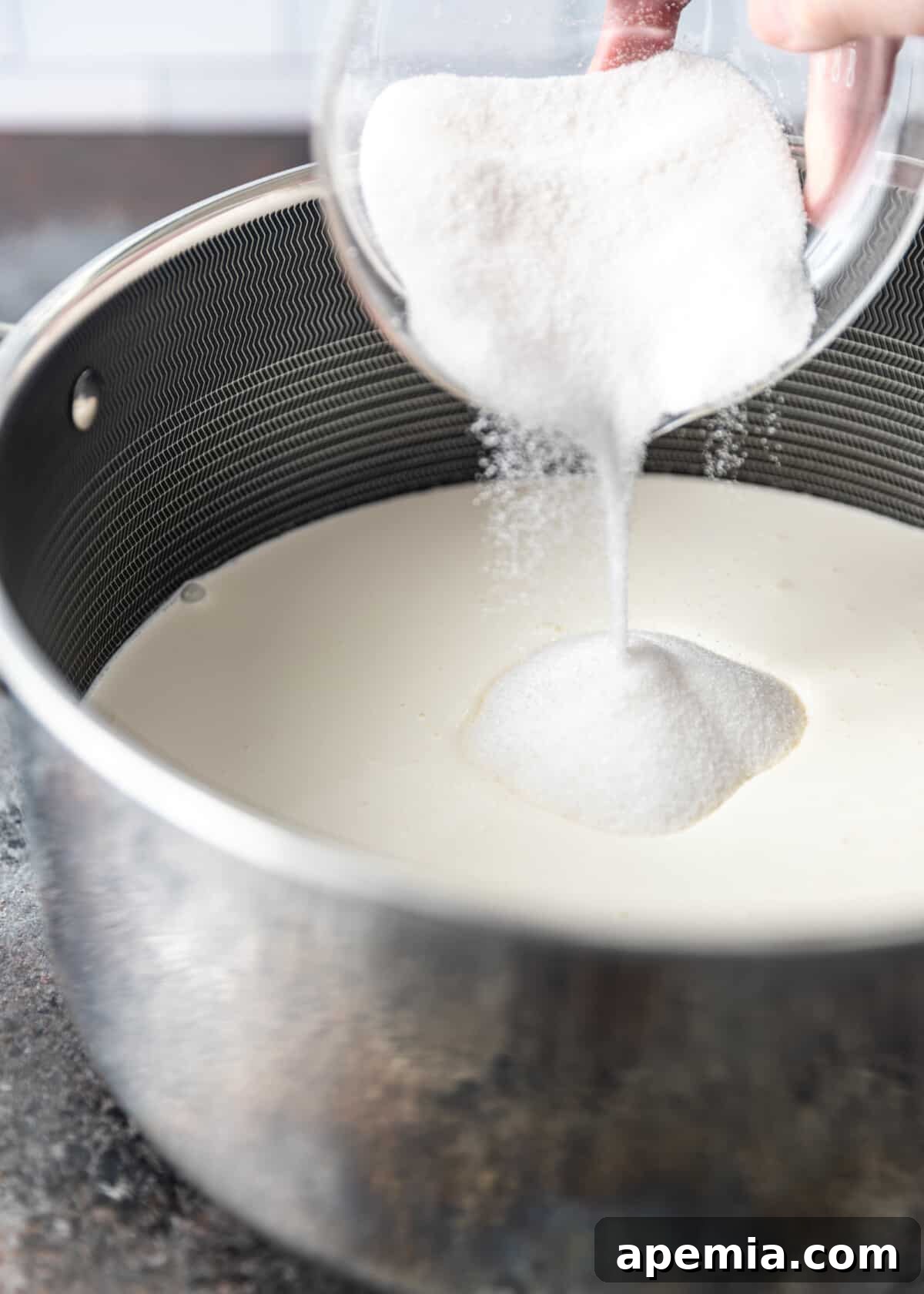 Zesty Creamy Lemon Posset 5 Adding granulated sugar to a pot filled with heavy cream.