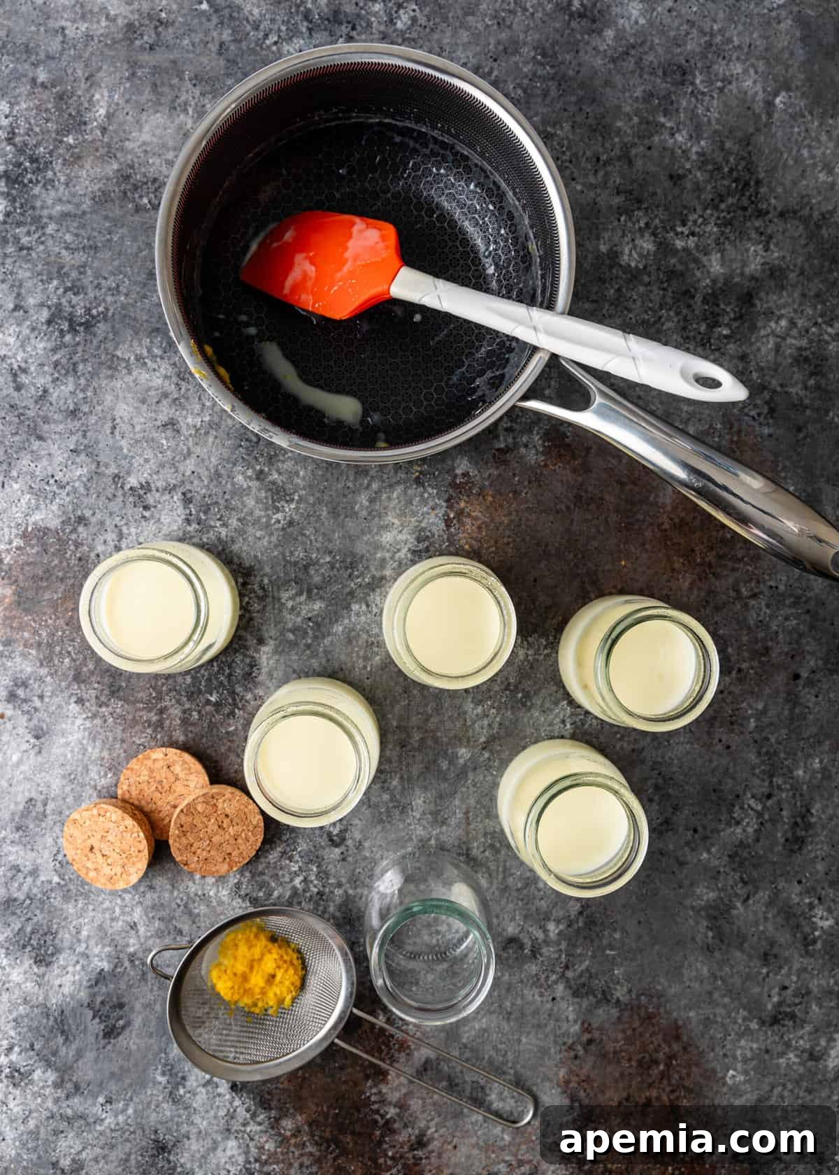 Zesty Creamy Lemon Posset 7 Overhead shot of the posset making process, showing a saucepan, small glass jars for serving, and a strainer with lemon zest.