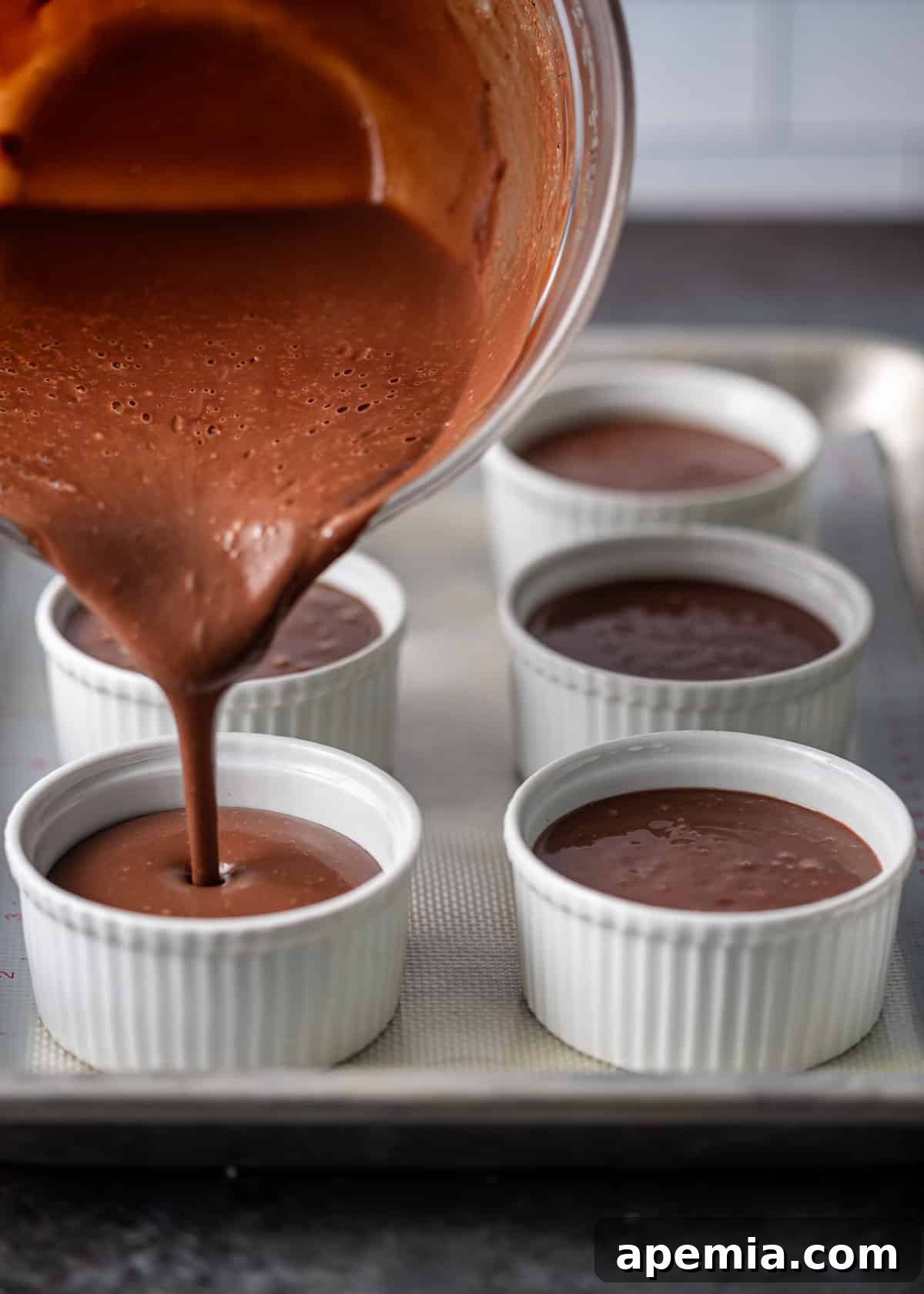 Decadent Chocolate Pots de Crème 5 side view: expertly pouring the smooth pots de creme batter into small white ramekins arranged on a baking sheet, illustrating the preparation process