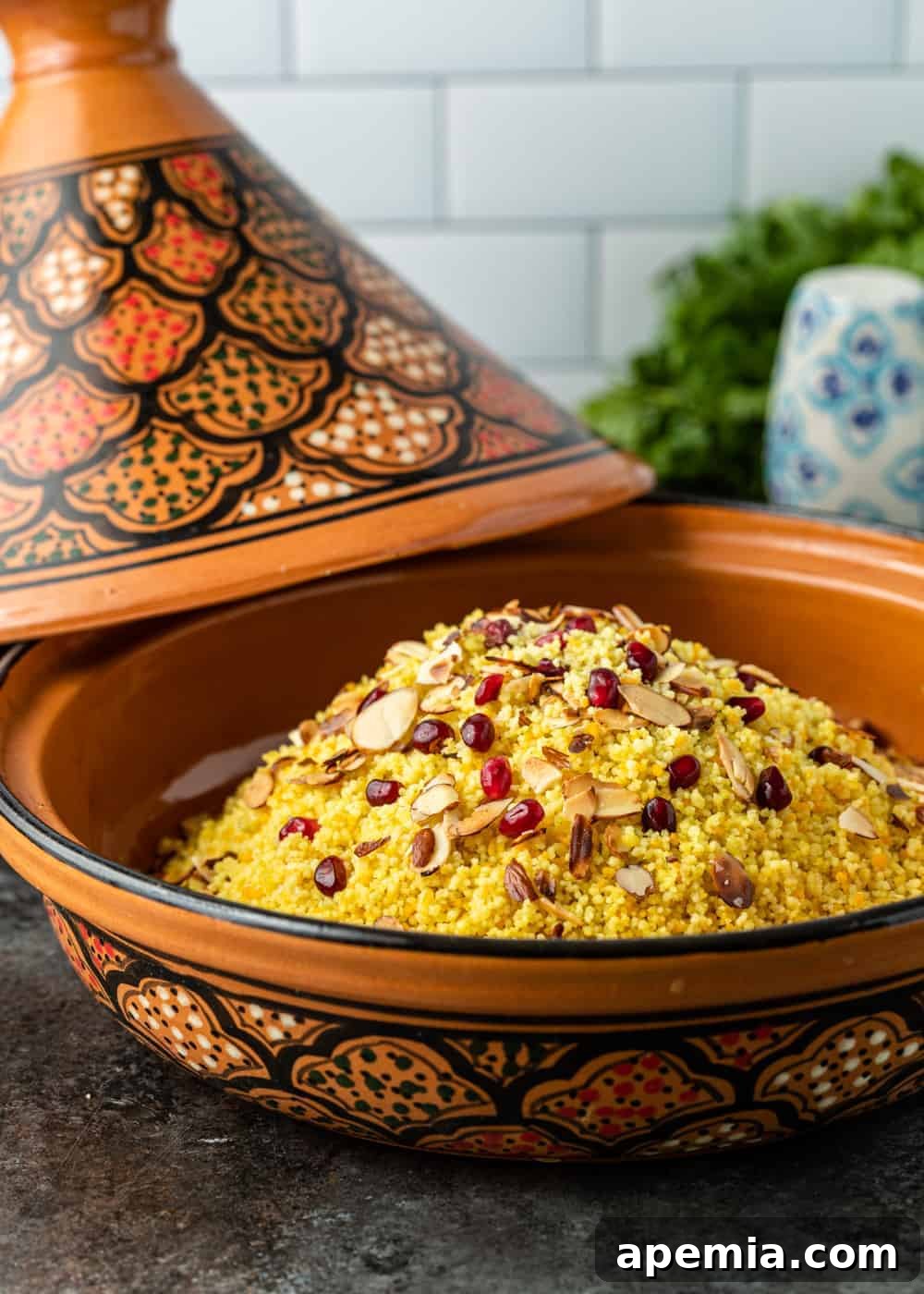 tagine filled with yellow pearled couscous side dish, garnished with pomegranate seeds and slivered almonds, ready to serve