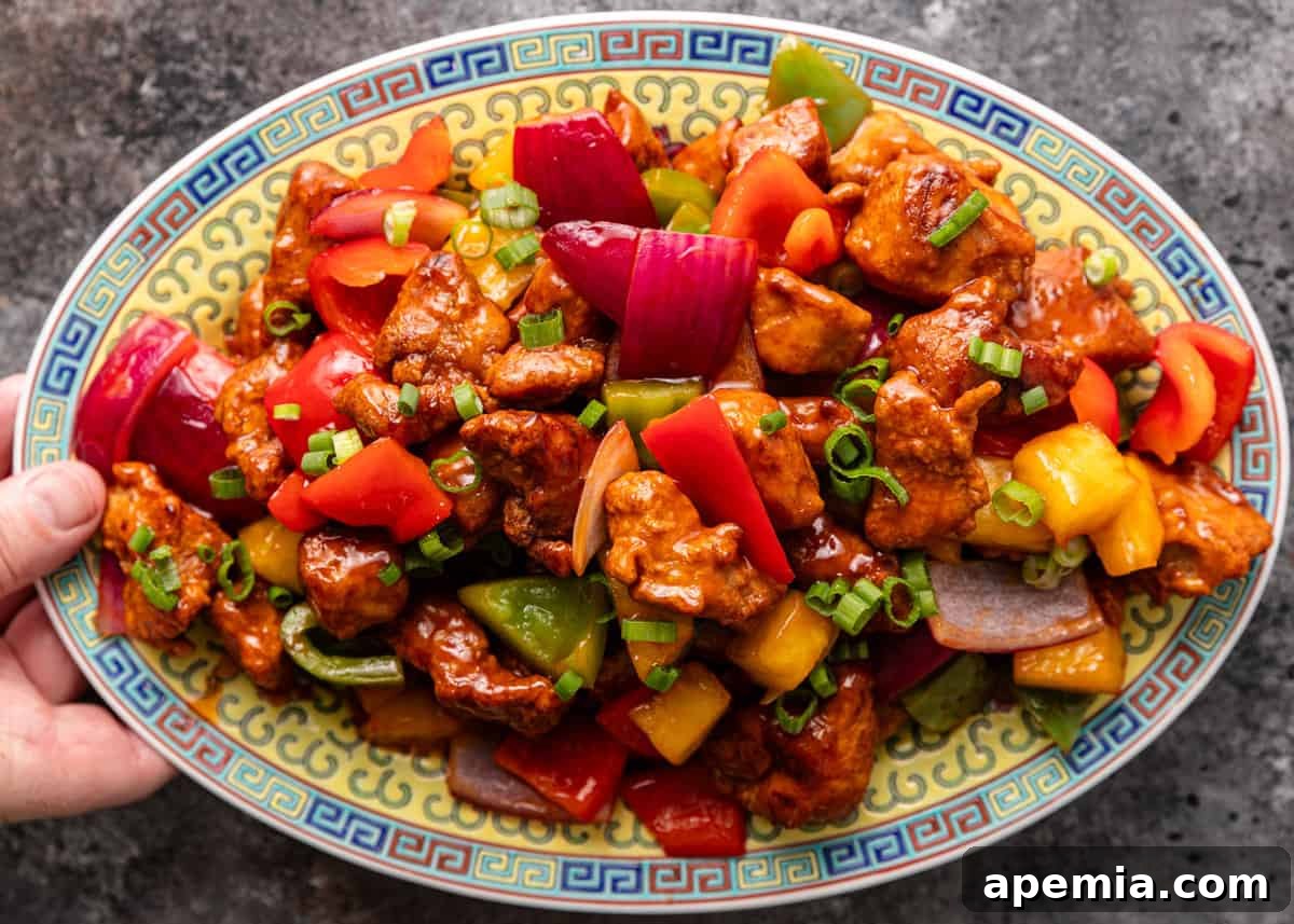 overhead: a hand holding a large platter of vibrant sweet and sour pork stir fry, ready to serve
