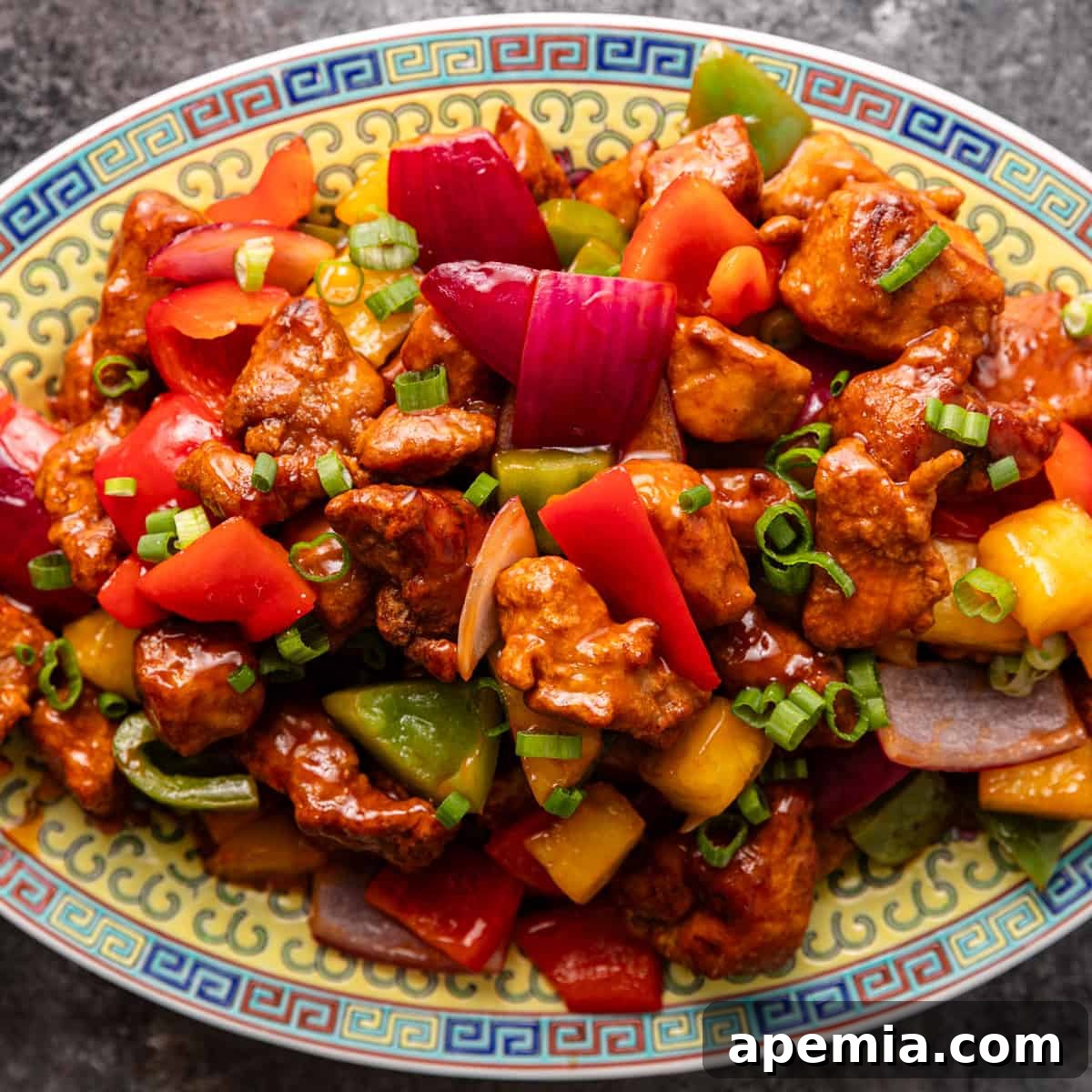 Overhead closeup of homemade sweet and sour chicken with vibrant bell peppers and green onions on a ceramic serving dish, ready to be enjoyed.