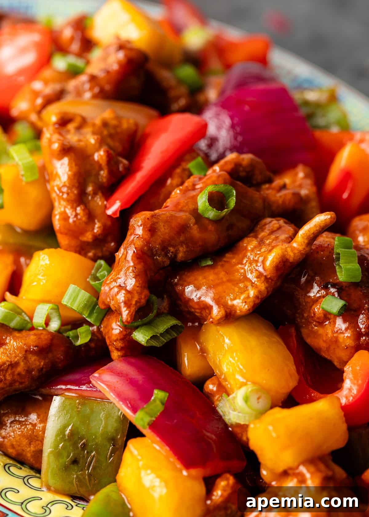Extreme closeup showing crispy sweet and sour chicken pieces, vibrant red bell peppers, and fresh green onions, showcasing the dish's irresistible texture and color.