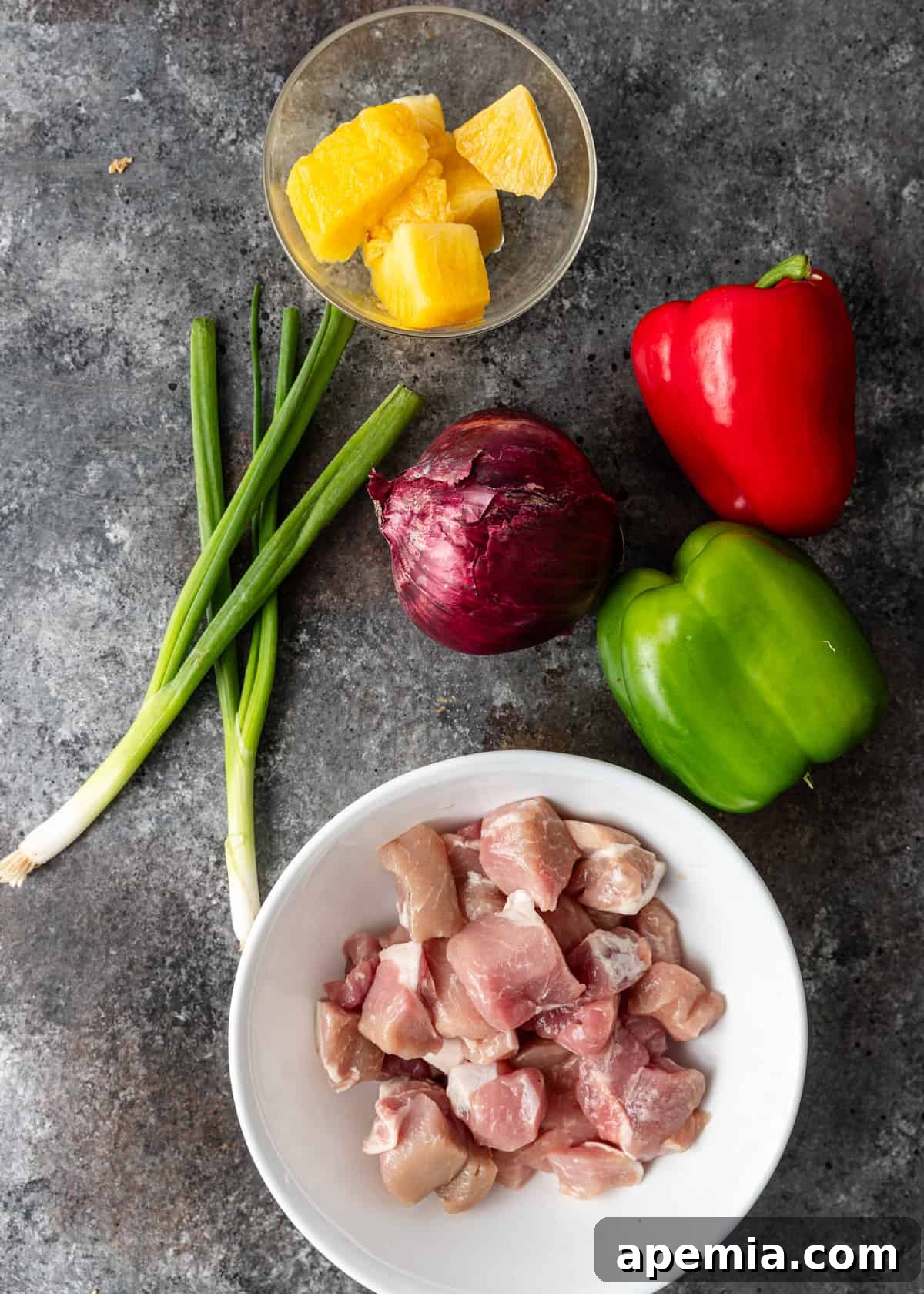 Overhead shot of all fresh ingredients laid out for sweet and sour chicken stir-fry, highlighting colorful bell peppers, pineapple, and chicken pieces.