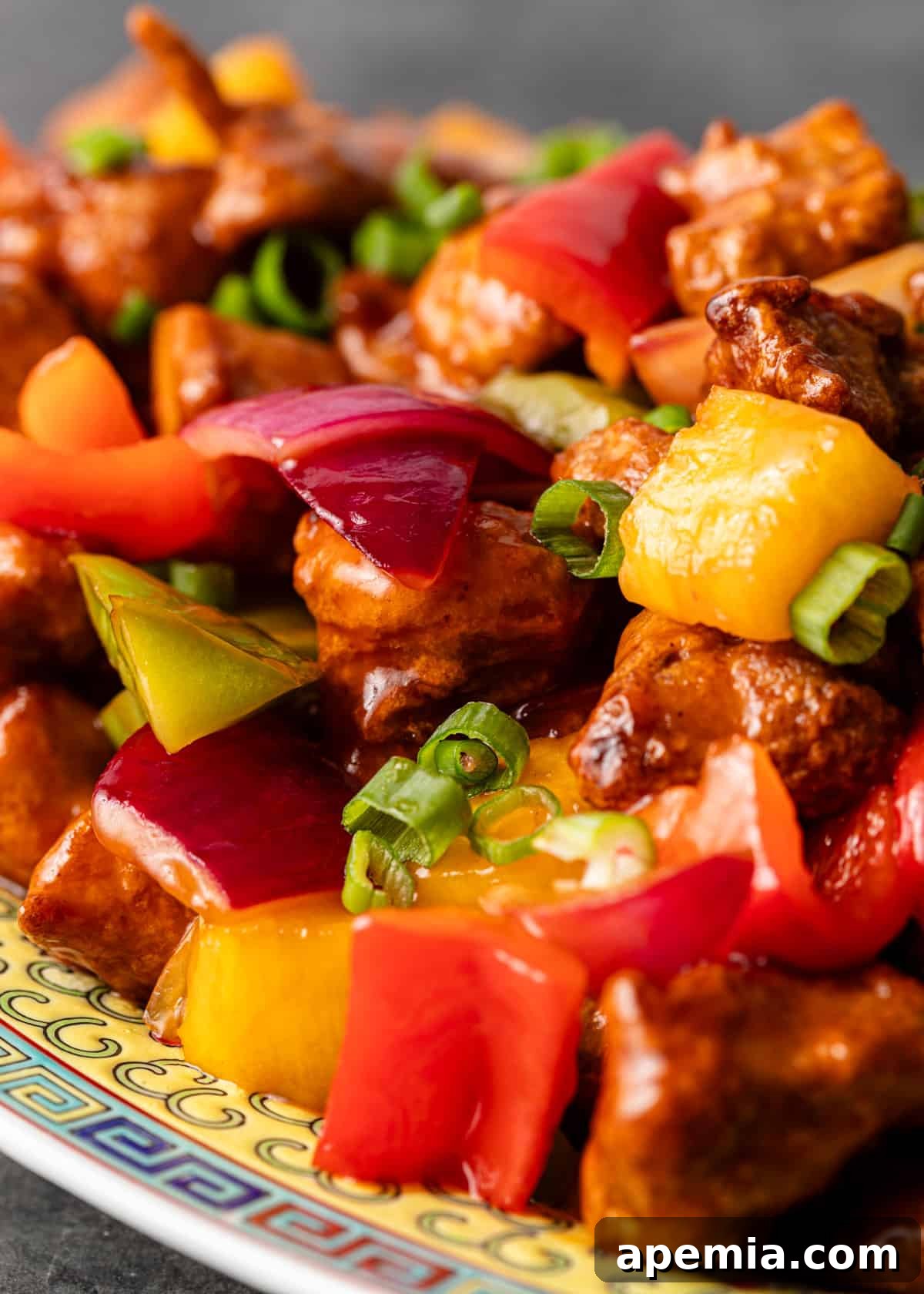 Extreme closeup of sweet and sour chicken stir-fry showcasing vibrant red onion, crisp bell peppers, and fresh green onion garnish, highlighting the dish's colorful appeal.