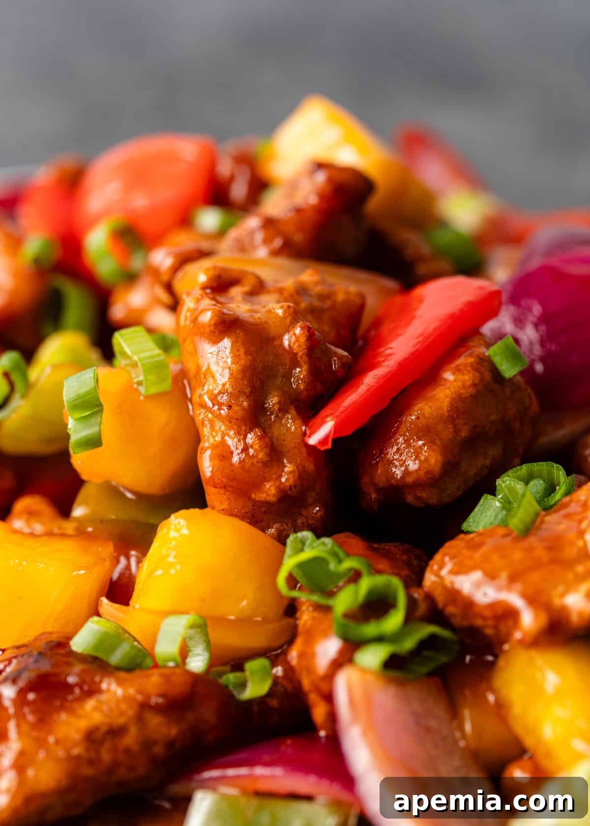 Extreme closeup of sweet and sour chicken stir-fry featuring perfectly coated chicken, colorful vegetables, and a sprinkle of fresh green onion, showcasing its delicious appearance.