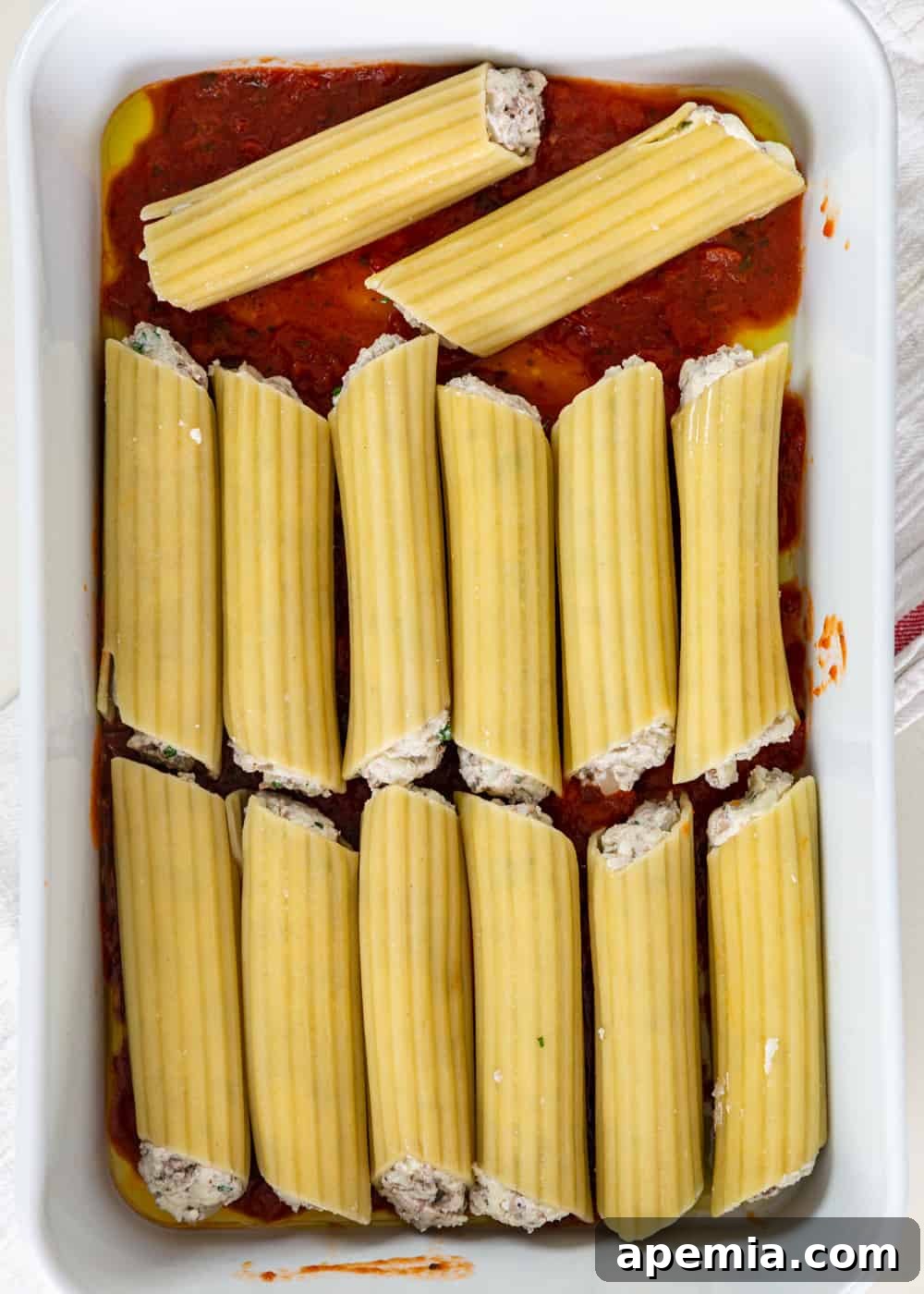 overhead process shot: stuffed manicotti tubes arranged in a baking dish over marinara sauce, before baking