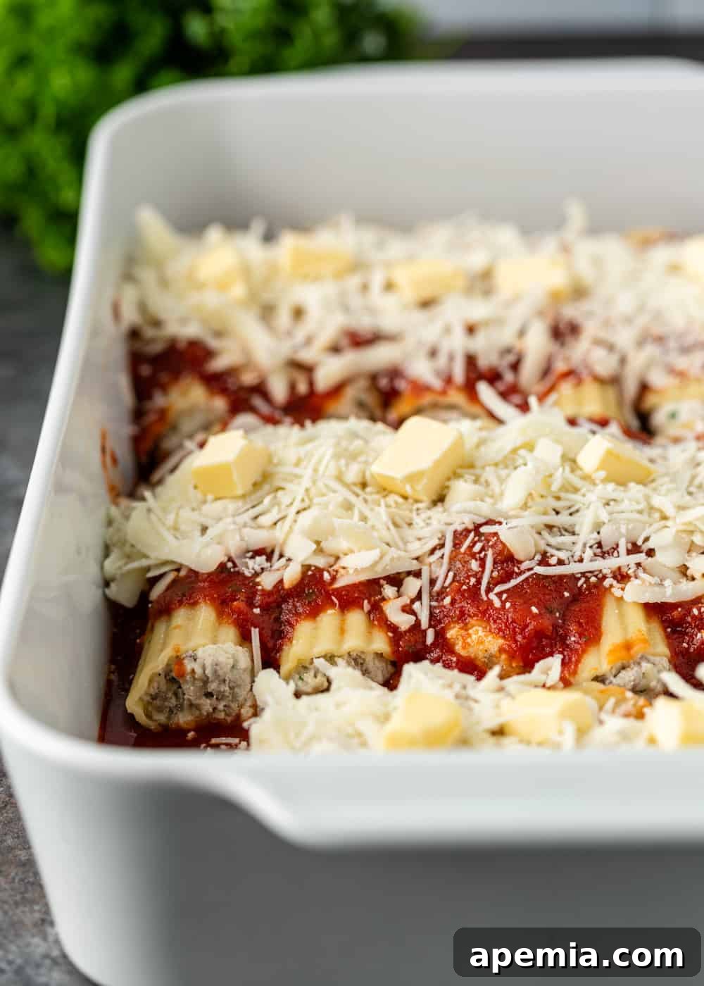 unbaked authentic italian manicotti in a baking dish, topped with sauce, cheese, and butter pieces