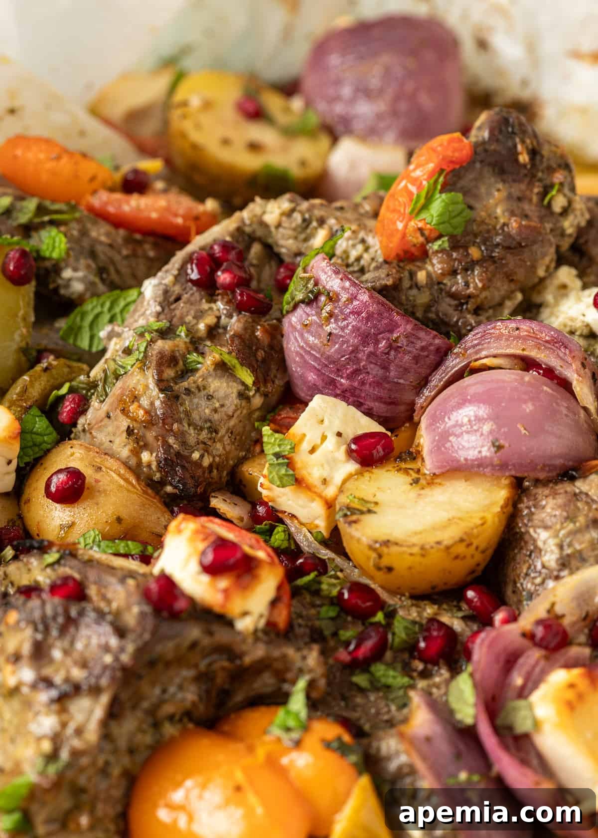 Roasted Kleftiko in a pan, showcasing tender lamb, golden potatoes, onions, fresh parsley, and bright pomegranate seeds