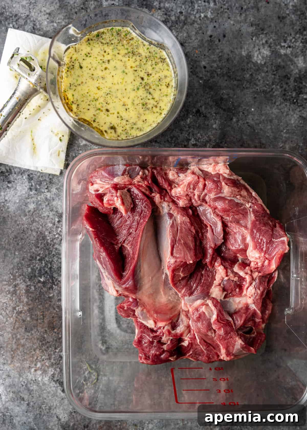 Overhead shot of Greek lamb in a plastic measuring bowl with marinade to the side, ready for marination