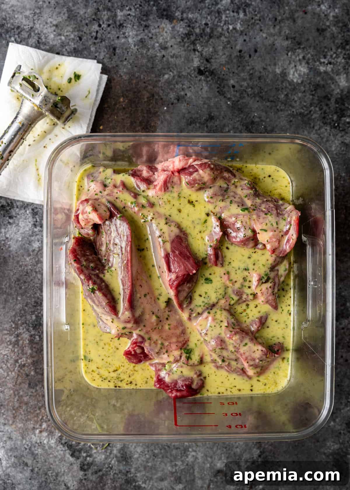 Overhead shot of kleftiko marinating in a large plastic measuring bowl, coated in a vibrant herb mixture