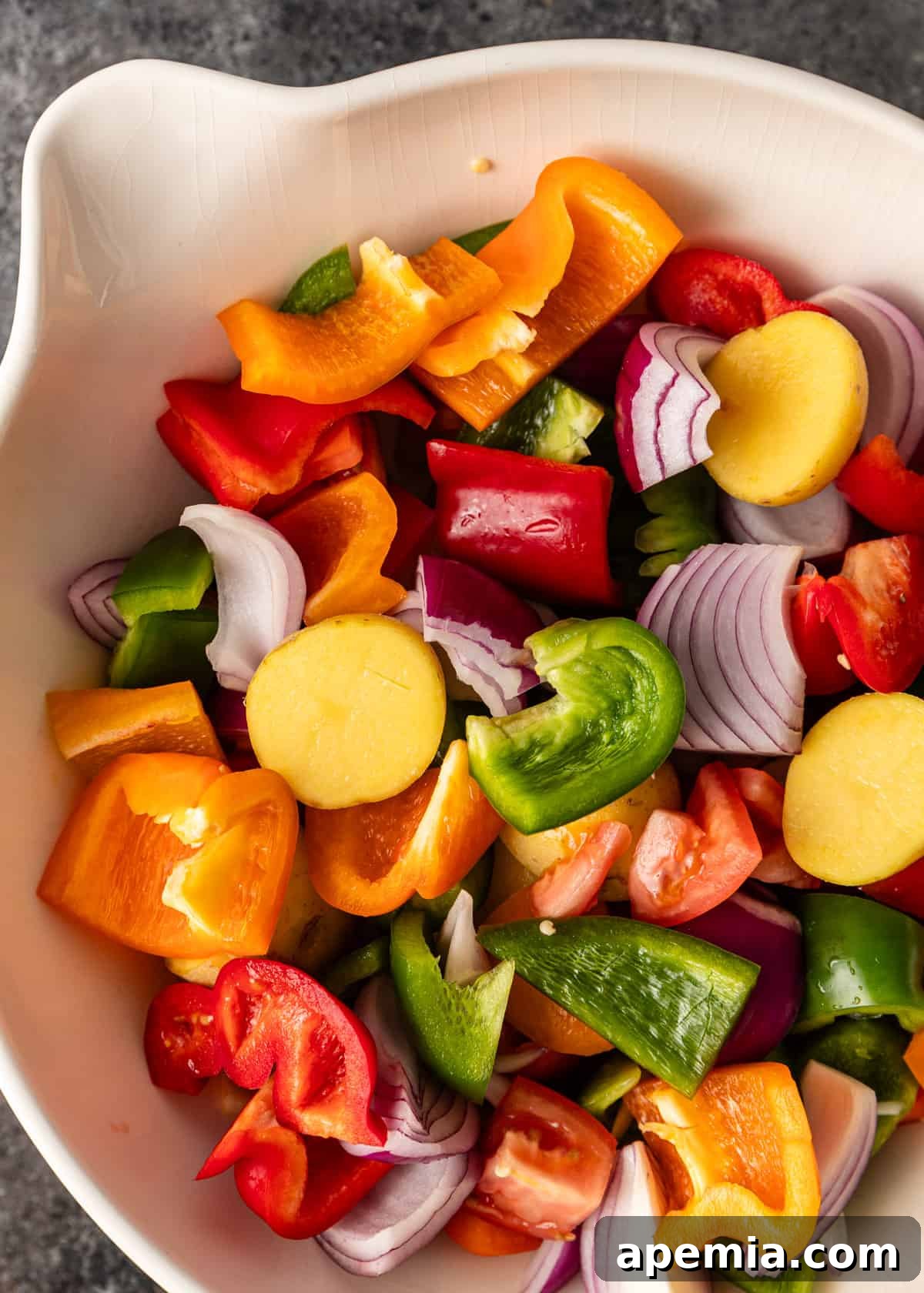 Overhead shot of freshly chopped vegetables, including potatoes, bell peppers, onions, and tomatoes, in a mixing bowl