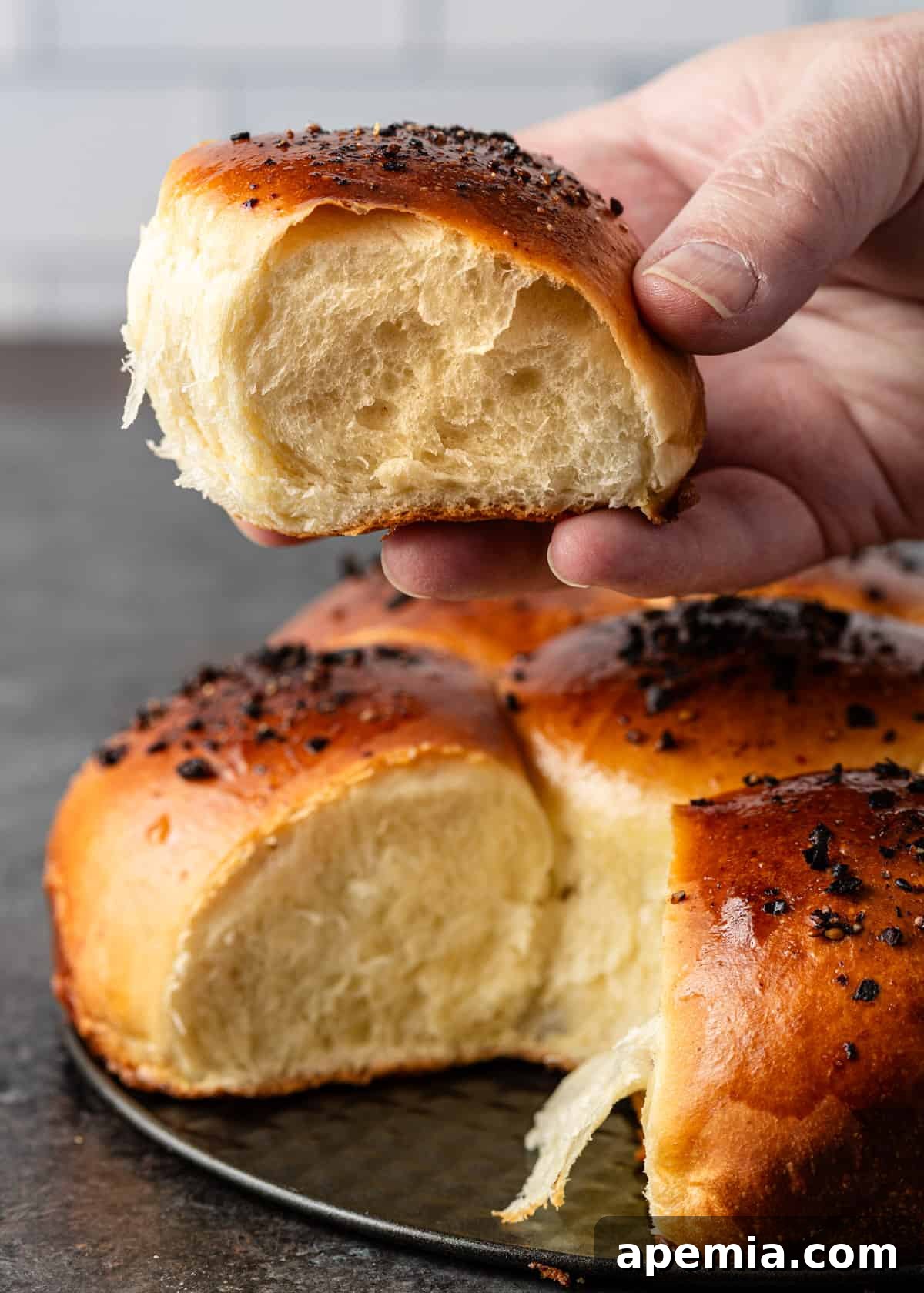 Closeup of a hand gently lifting a piece of Japanese milk bread from the baking pan, highlighting its soft texture.