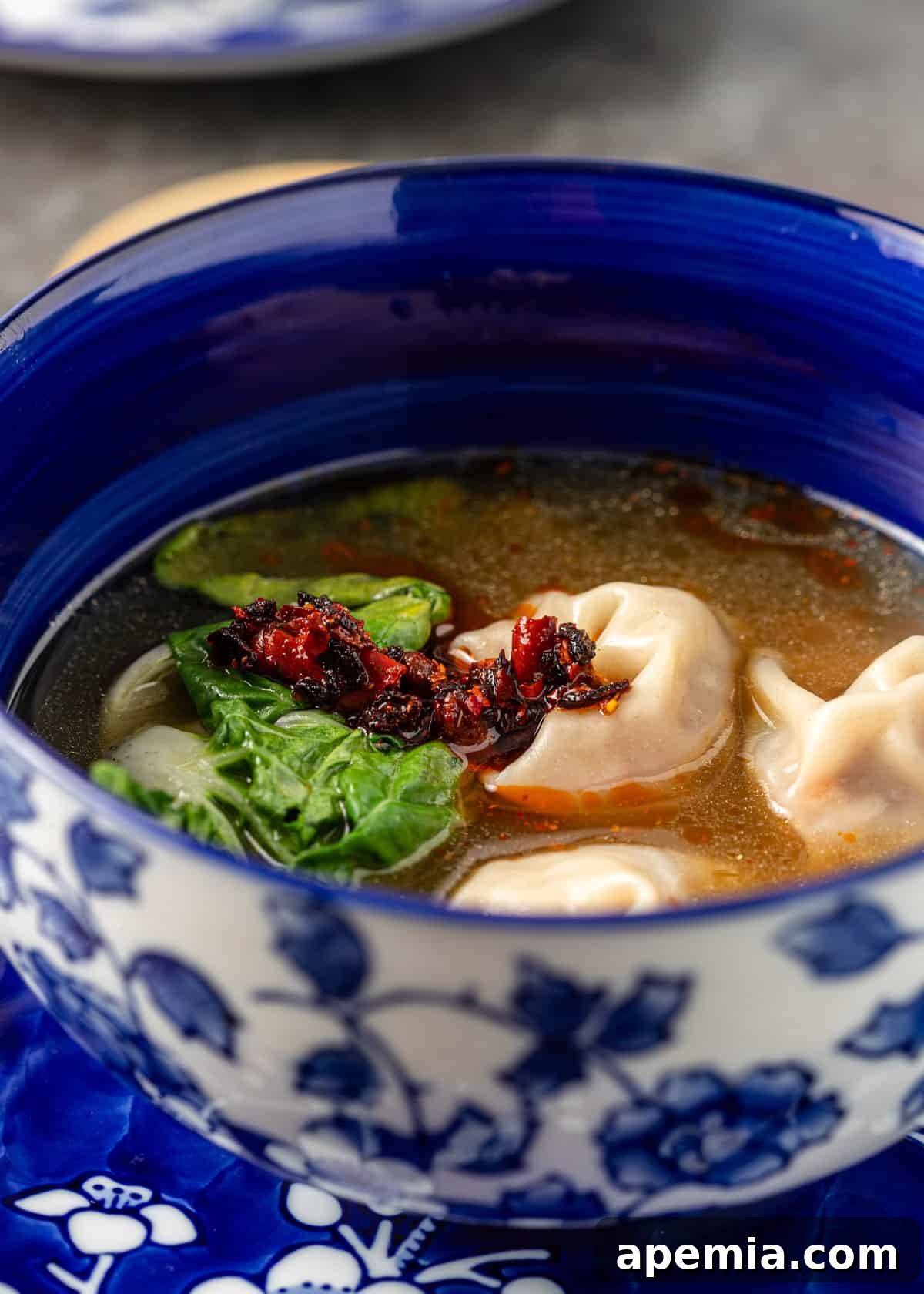 side view: a blue bowl of wonton soup with chili paste and bok choy on top