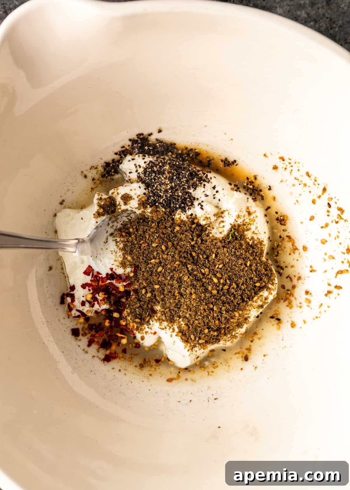 Overhead view of a mixing bowl containing the creamy yogurt marinade ingredients being whisked together.