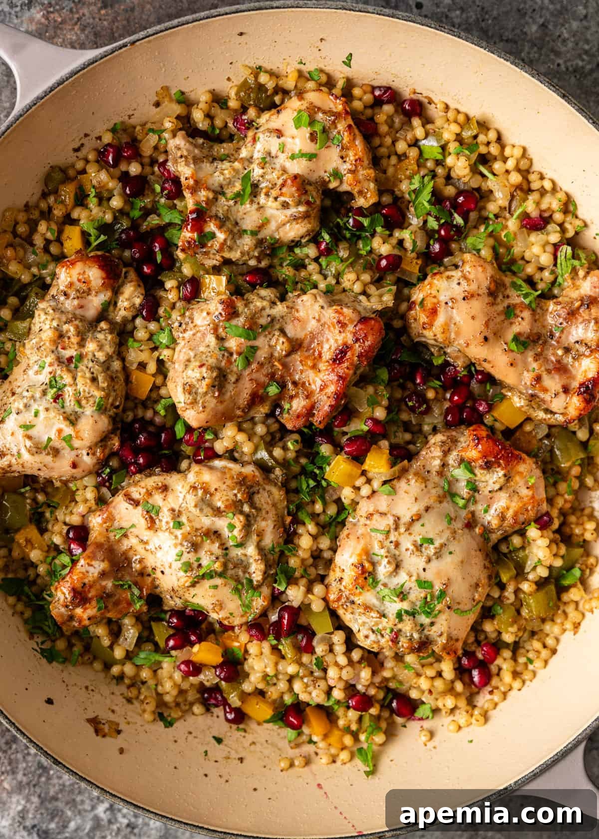 Overhead view of a baked za'atar yogurt chicken recipe served over pearl couscous, garnished with vibrant pomegranate seeds.