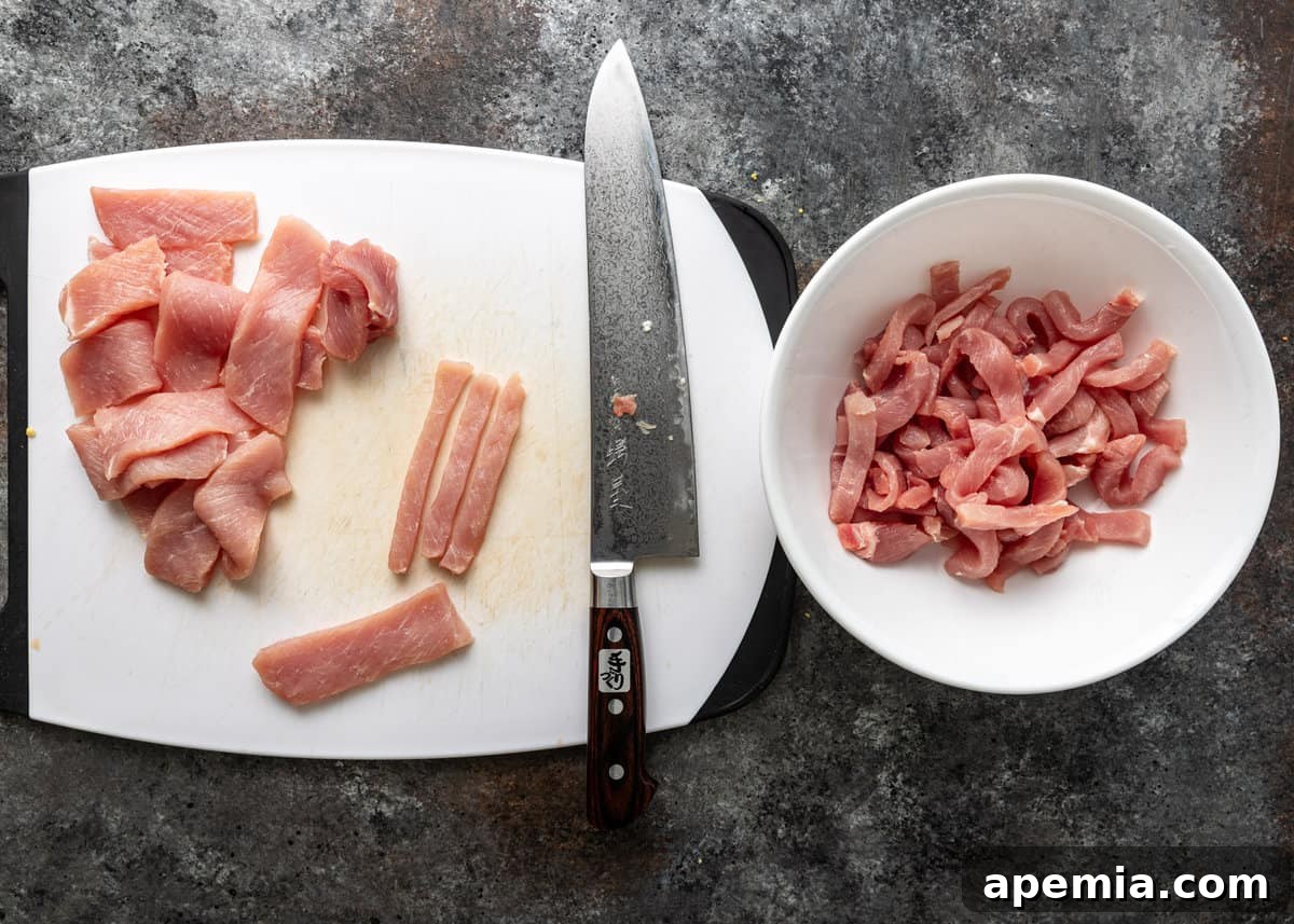 overhead: slicing pork on a white cutting board for vinegar pork stir fry