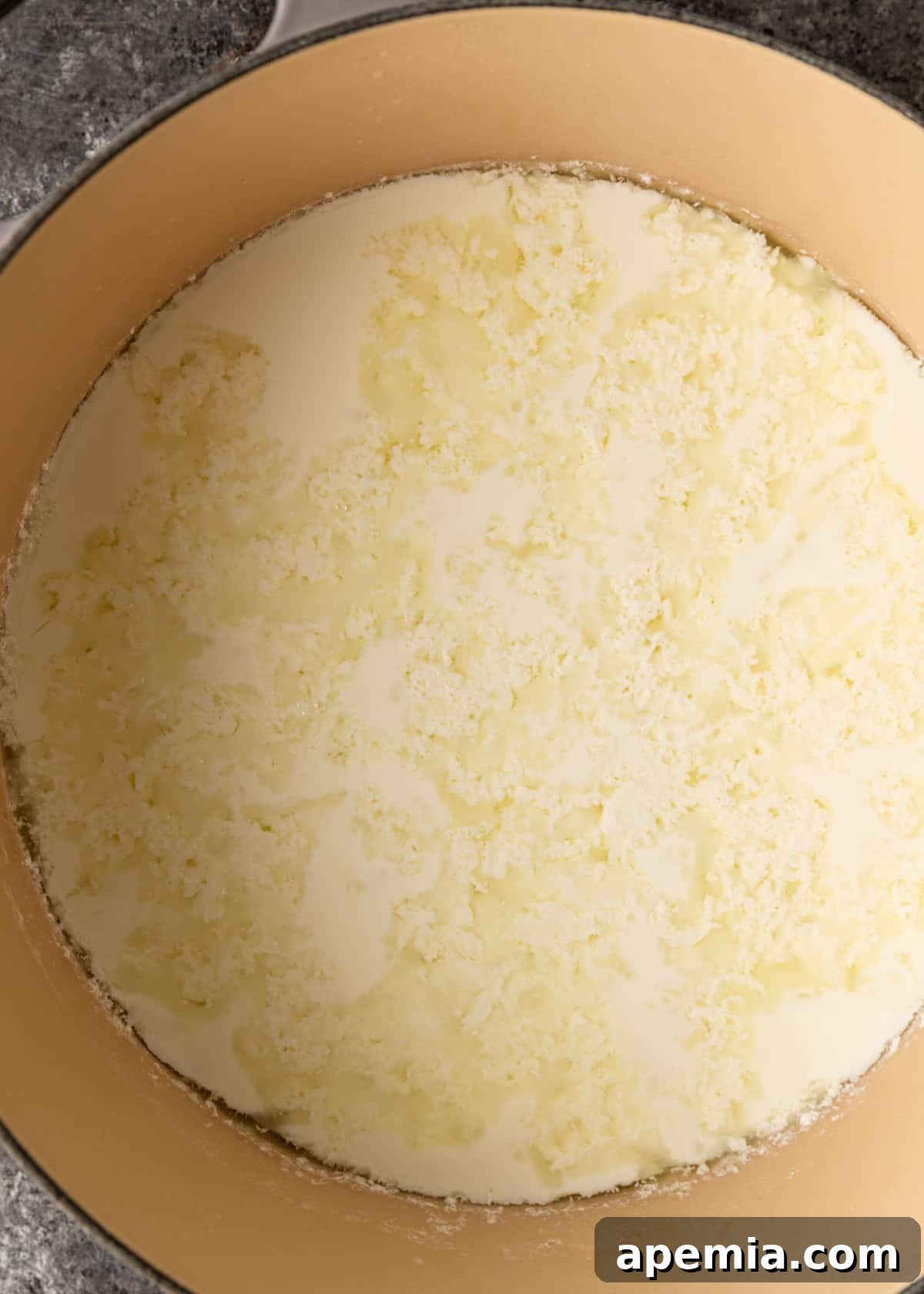 Overhead process shot: The whey and curd for Jibneh Arabieh separating clearly in a large pot, showing distinct yellow liquid and white solids.