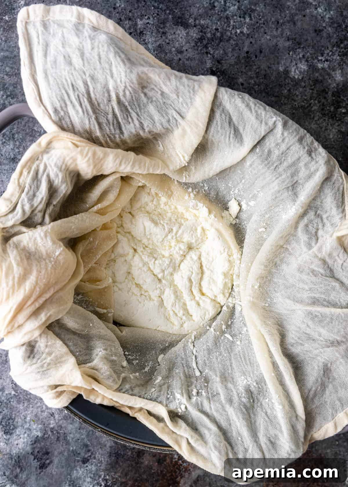 Overhead process shot: Straining and molding the cheese curd for Jibneh in a colander lined with cheesecloth.