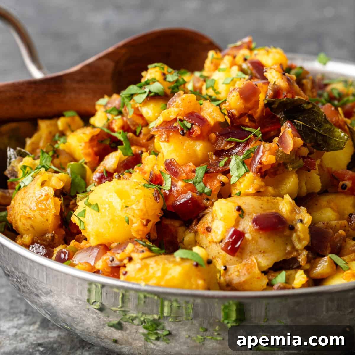 closeup: a large metal bowl full of potato curry, garnished with fresh cilantro