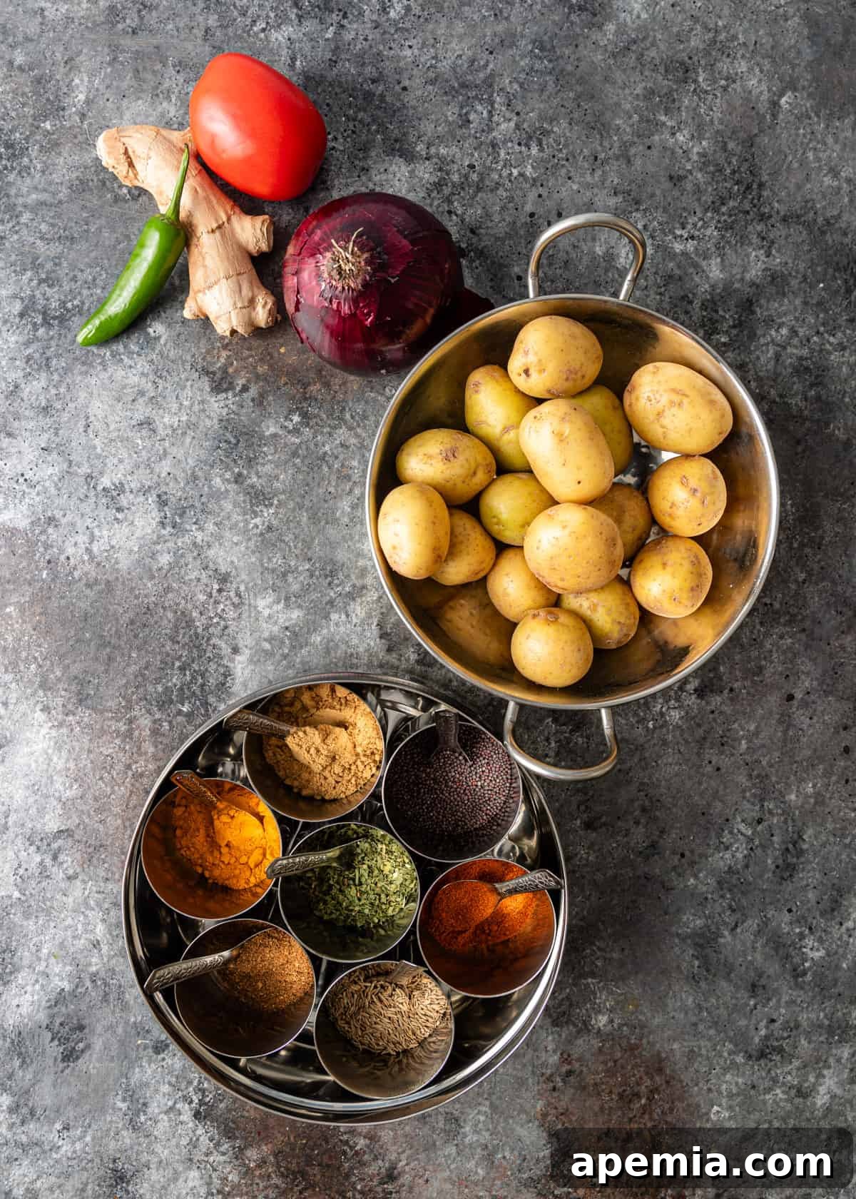 overhead: ingredients and spices needed for potato curry, laid out on a wooden board