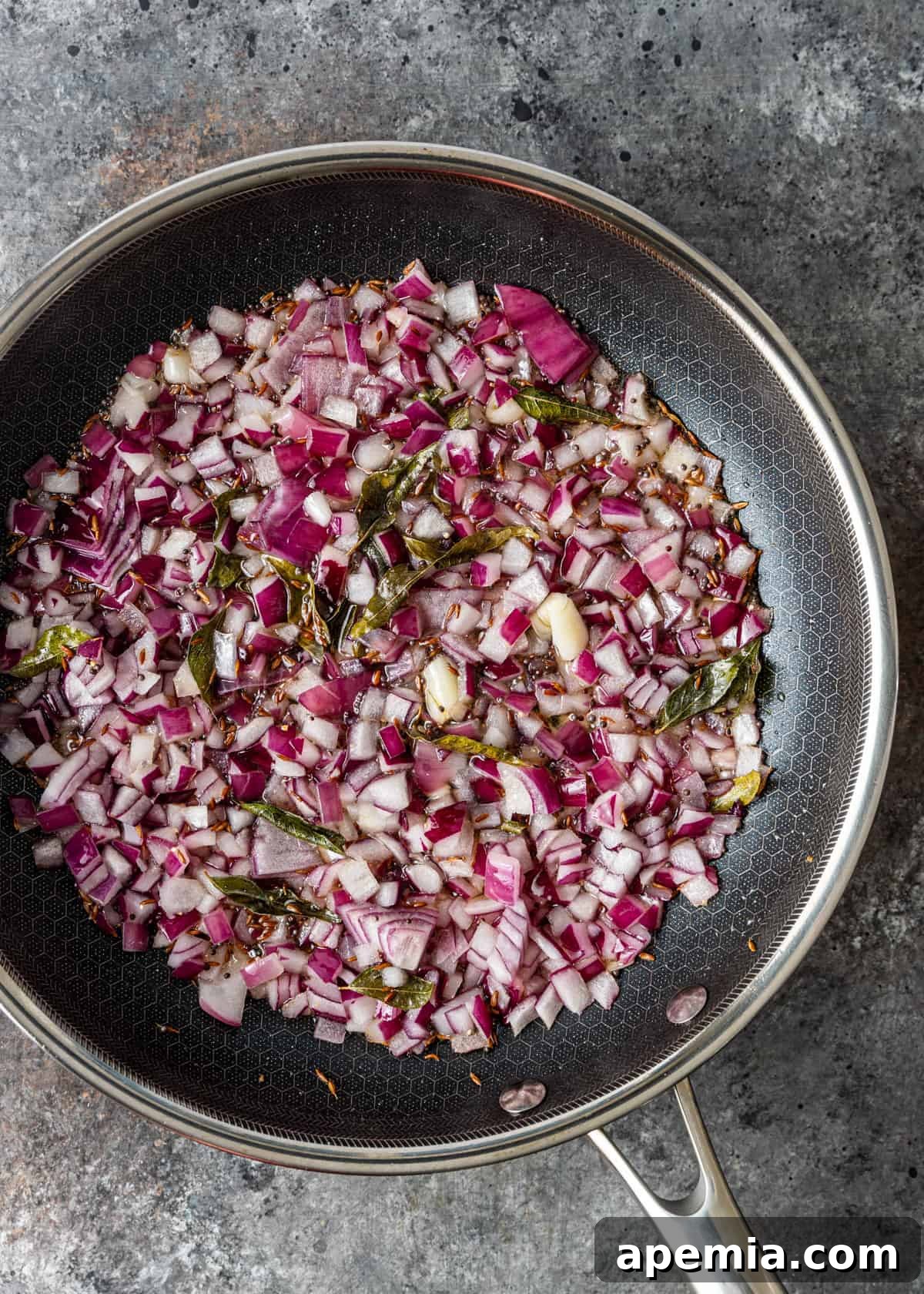 overhead process shot: tempered spices with red onion in a skillet