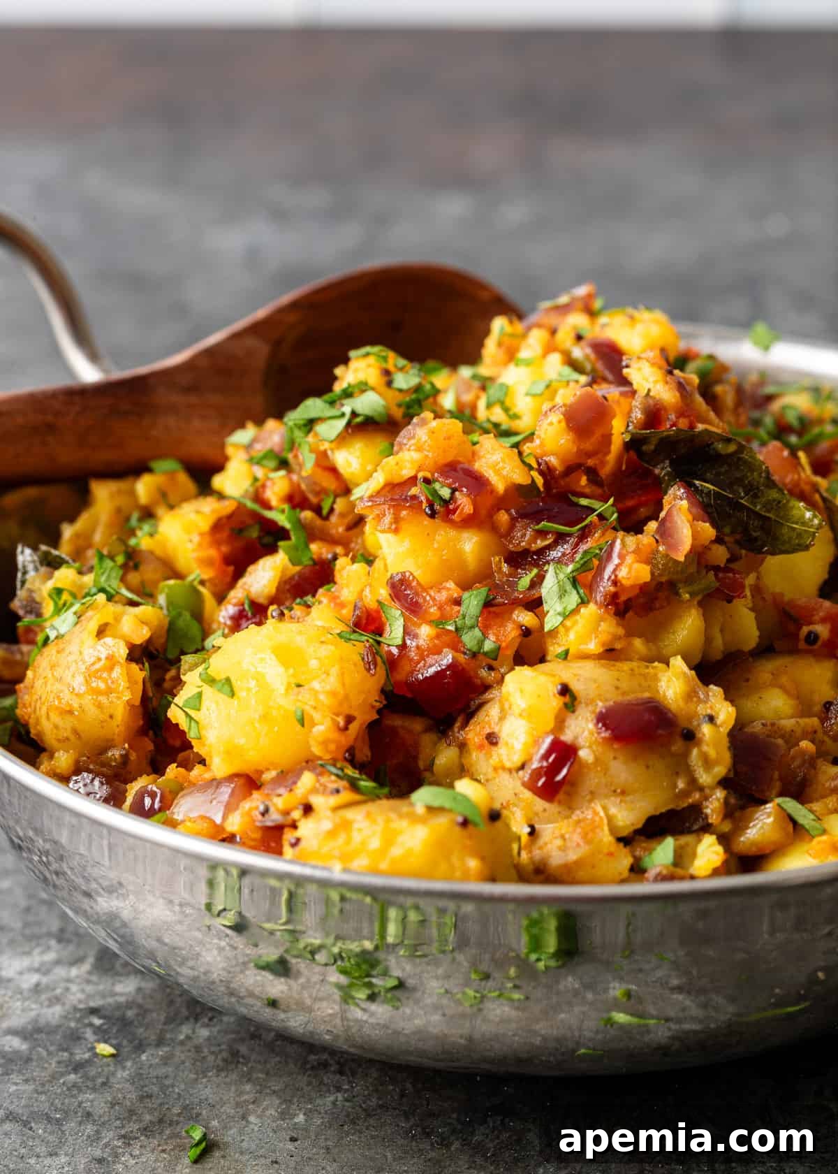 side view closeup: a large metal bowl full of potato curry with fresh herbs on top
