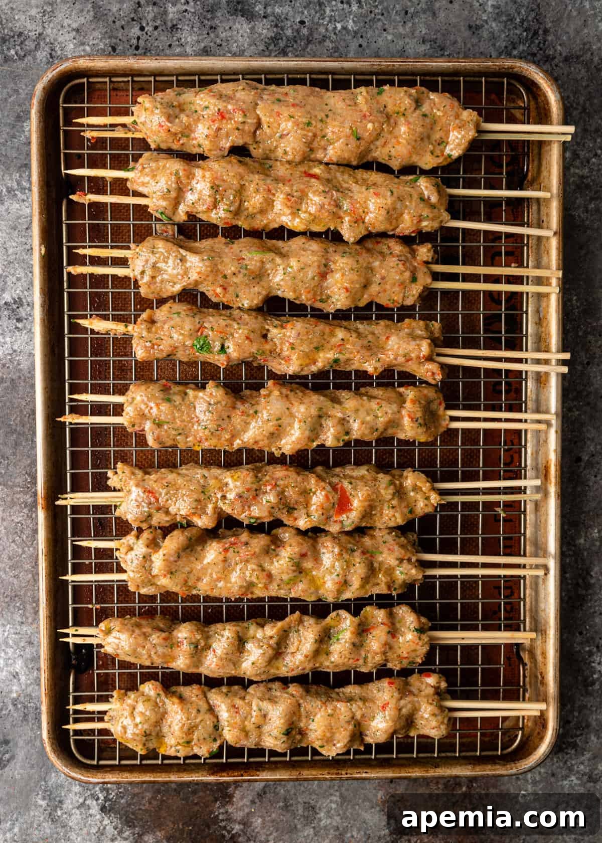 Overhead shot: chicken Adana mixture shaped onto skewers, resting on a wire rack over a baking sheet, ready for grilling