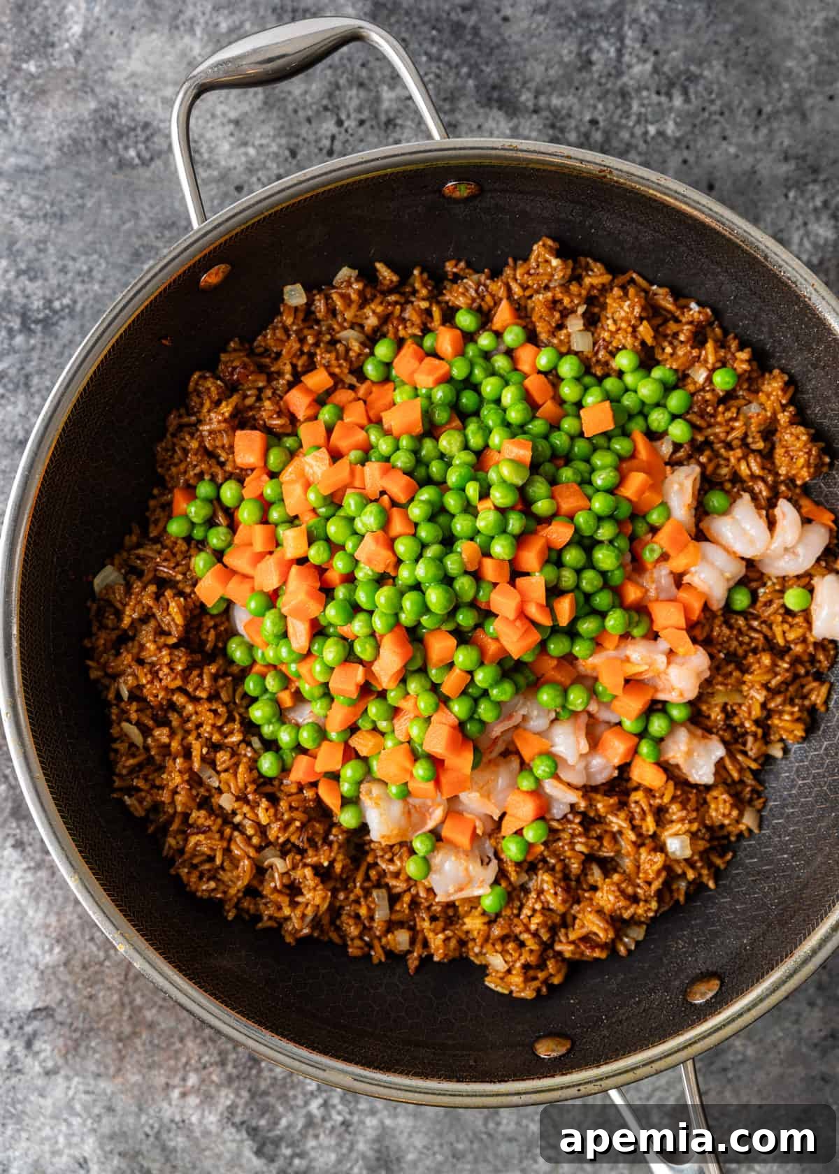 overhead process shot: adding vegetables and shrimp to rice in a large frying pan